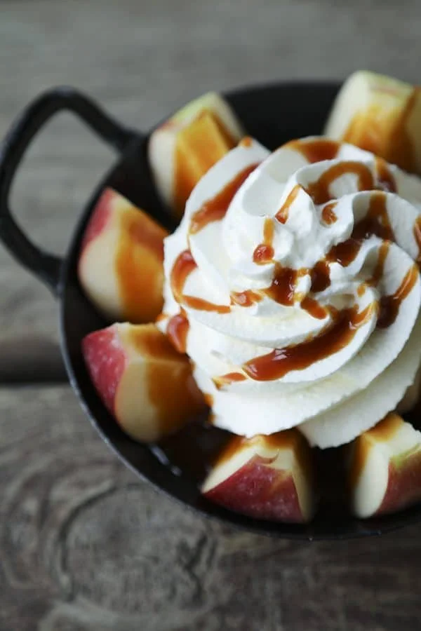 A small black skillet filled with sliced apples topped with whipped cream and caramel sauce.
