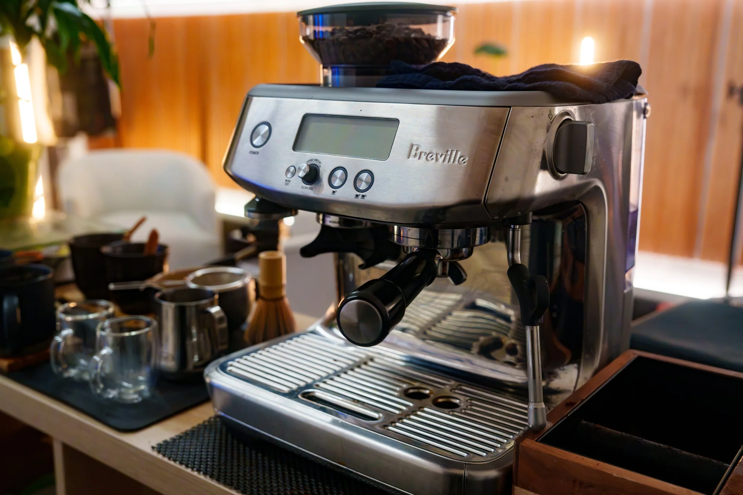 A Breville espresso machine on a kitchen counter, with cups and coffee-making accessories around it.