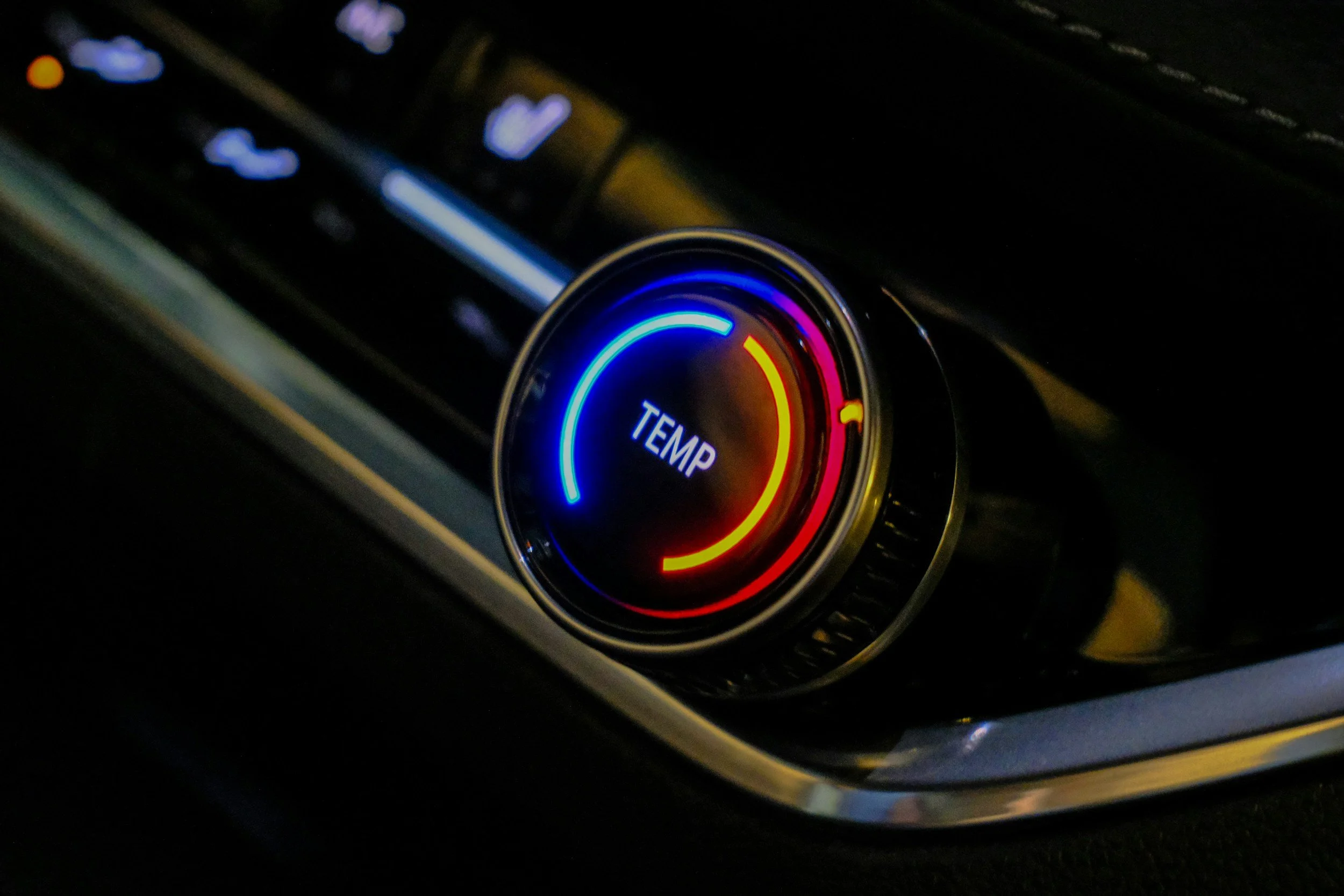 Car dashboard climate control panel with illuminated temperature dial showing warm temperature.
