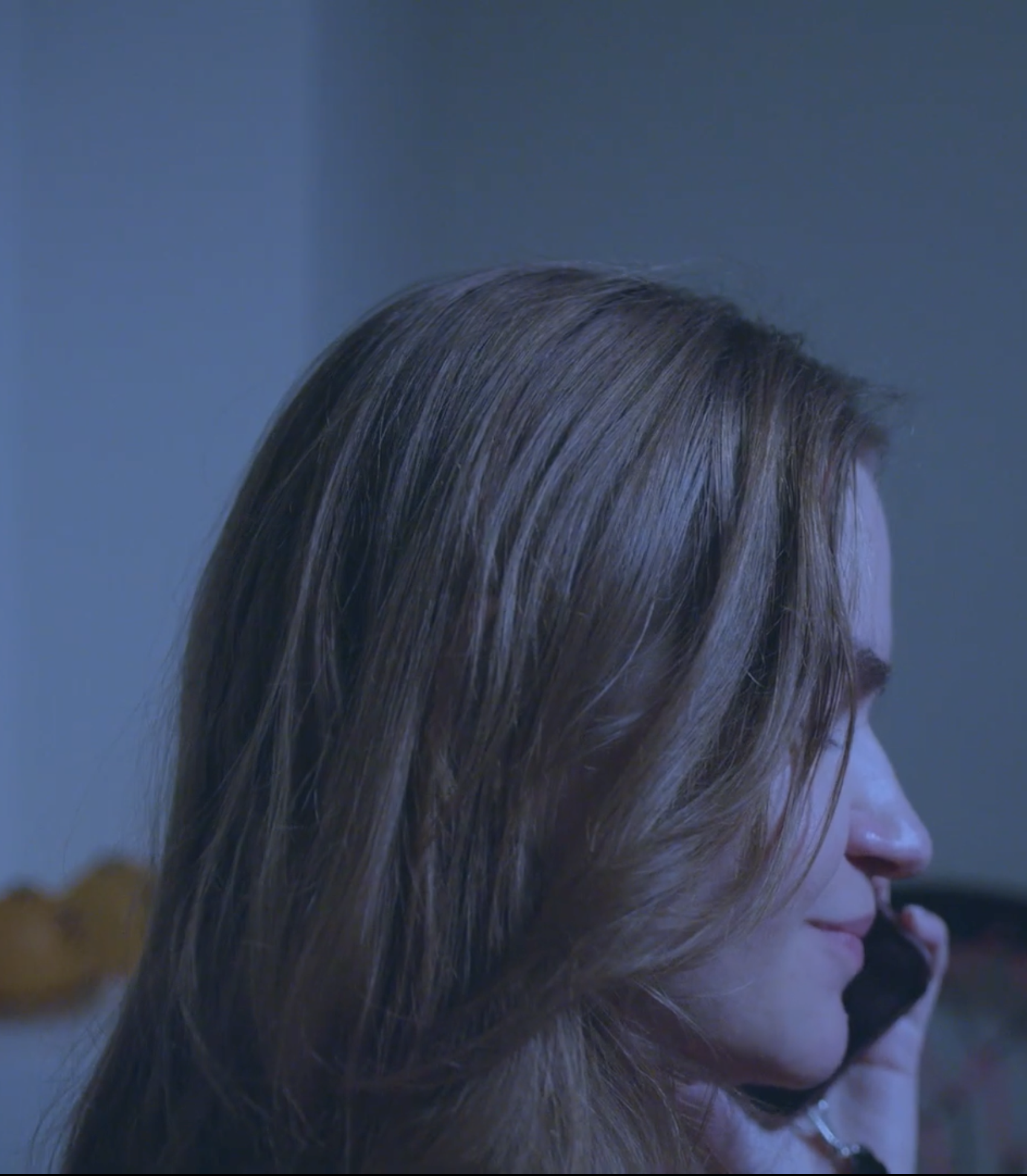 Side profile of a woman with long, brown hair, looking downward, with a calm facial expression.