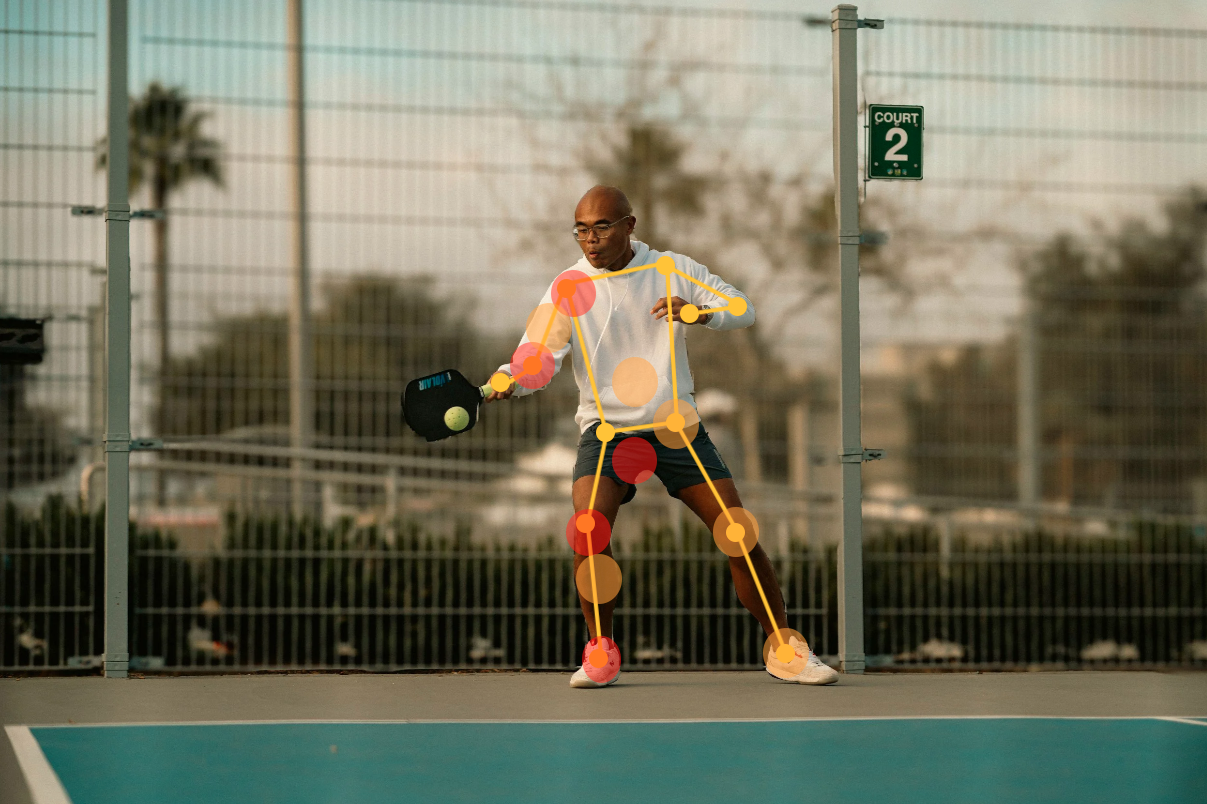 A man wearing glasses and athletic clothing is playing pickleball on an outdoor court, holding a paddle and hitting a ball.