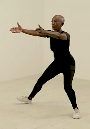 A woman practicing a yoga pose, standing with legs apart, arms extended forward, and head turned to the side in a minimalistic room.
