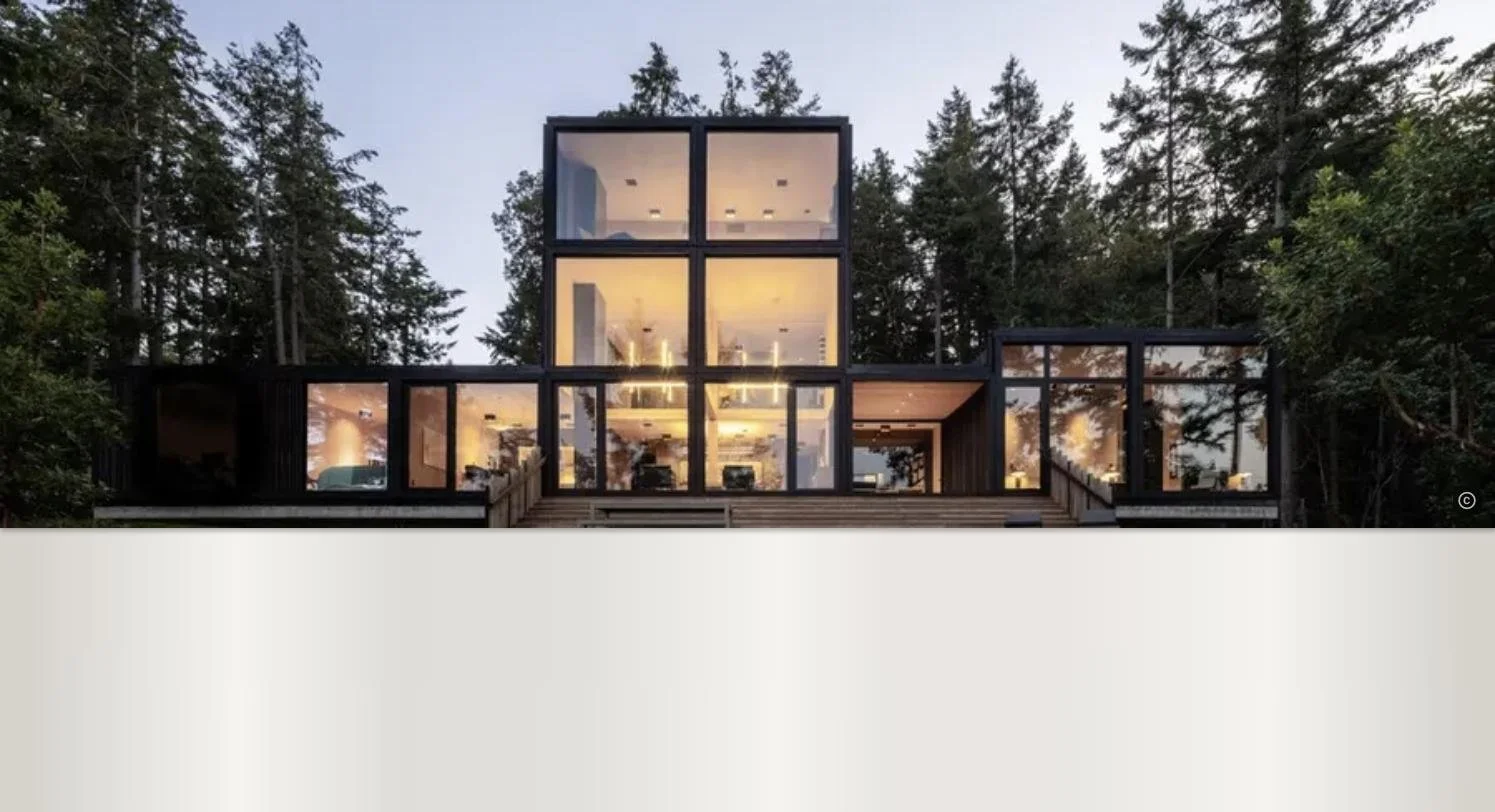 Modern house with large glass windows, surrounded by trees.