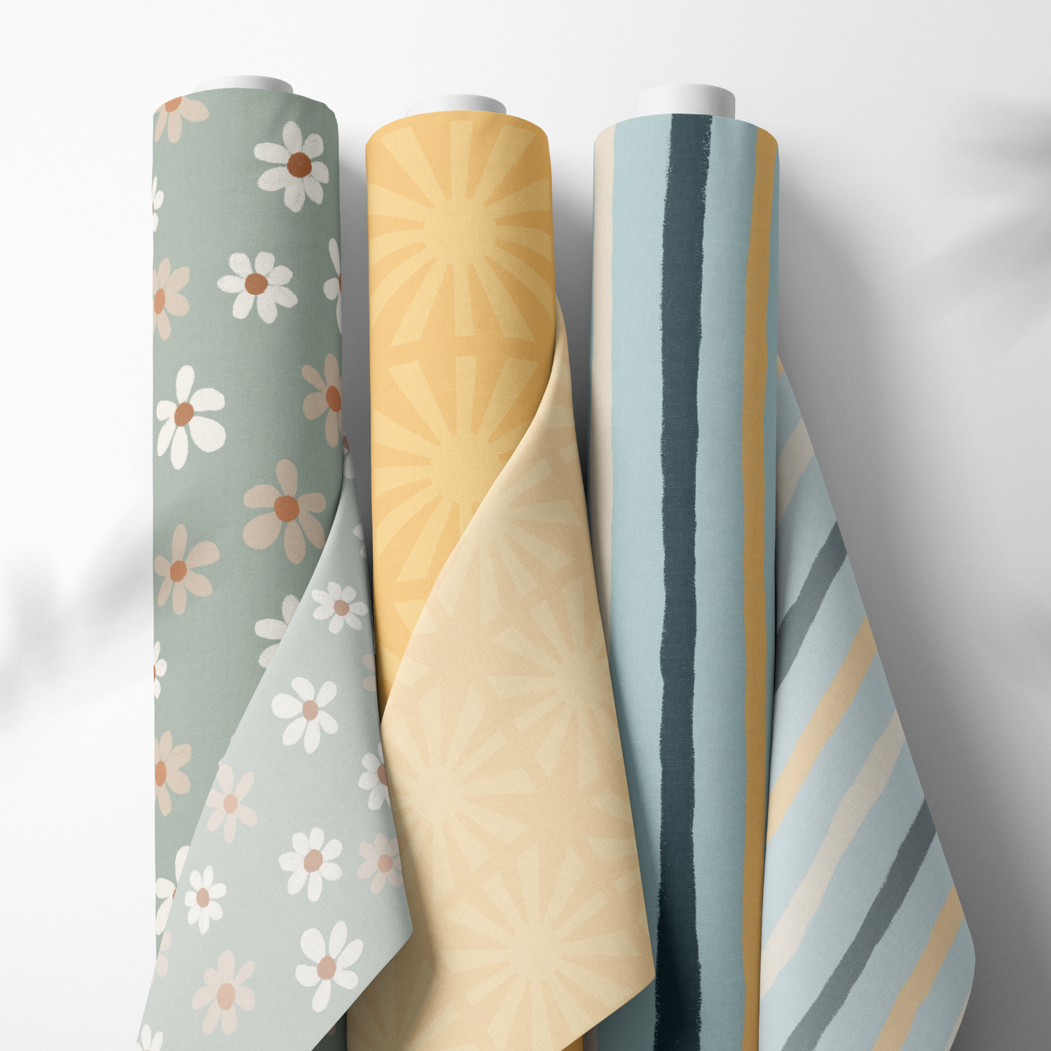 Five rolls of wallpaper with different patterns, from left to right: floral with daisies, yellow with sunburst design, blue with vertical stripes, and grey with diagonal stripes.