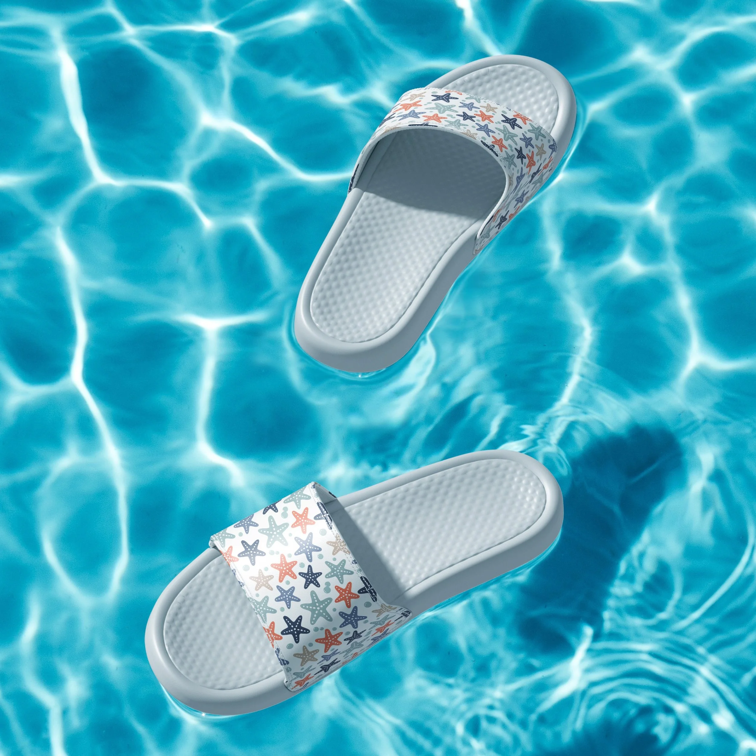 A white slip-resistant beach chair with stars and fish patterns on the fabric, floating in a swimming pool with clear blue water.