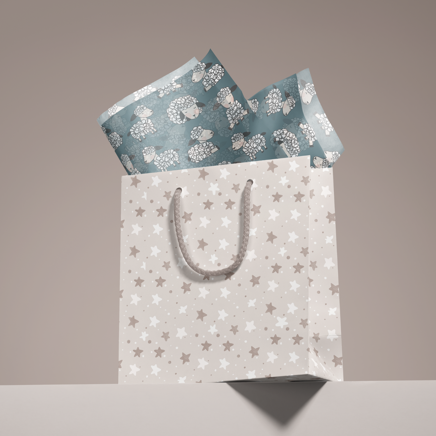 A white gift bag with star patterns and a gray rope handle, open to reveal blue tissue paper with sheep illustrations.