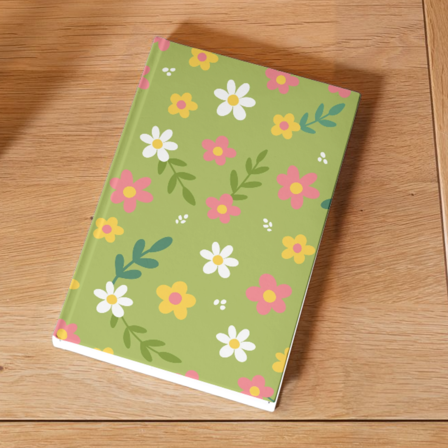 A closed notebook with a green cover decorated with white, pink, and yellow flowers and green leaves, placed on a wooden surface.