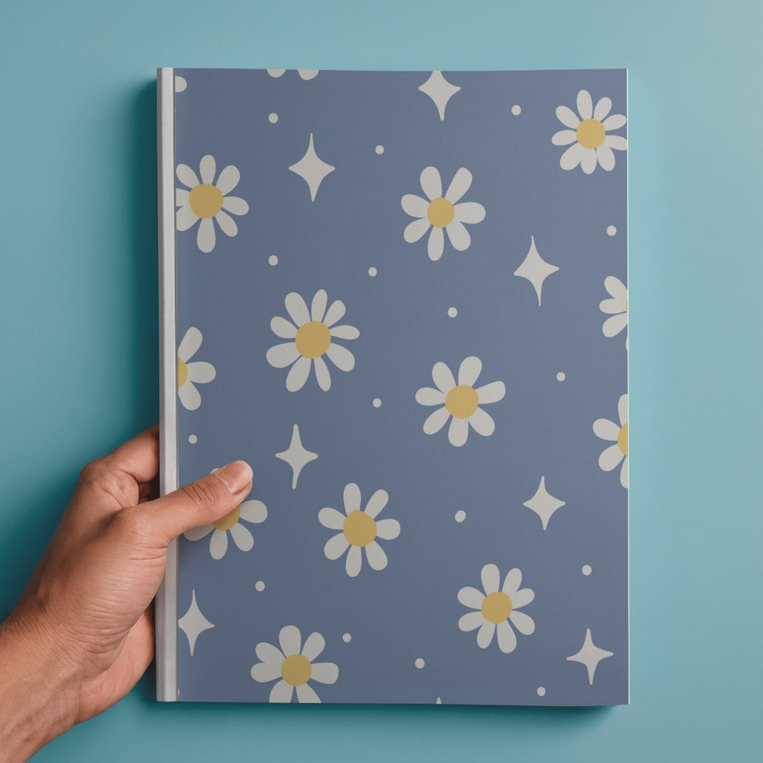 Person holding a notebook with a floral and star pattern cover against a blue background.