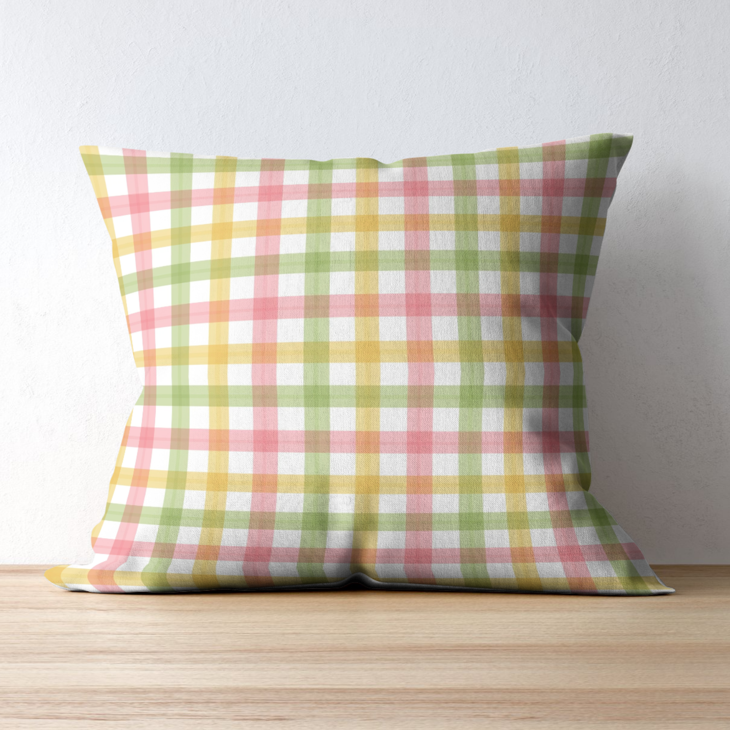 Colorful checkered pillow with pink, yellow, and green squares placed on a light wooden surface against a white wall.
