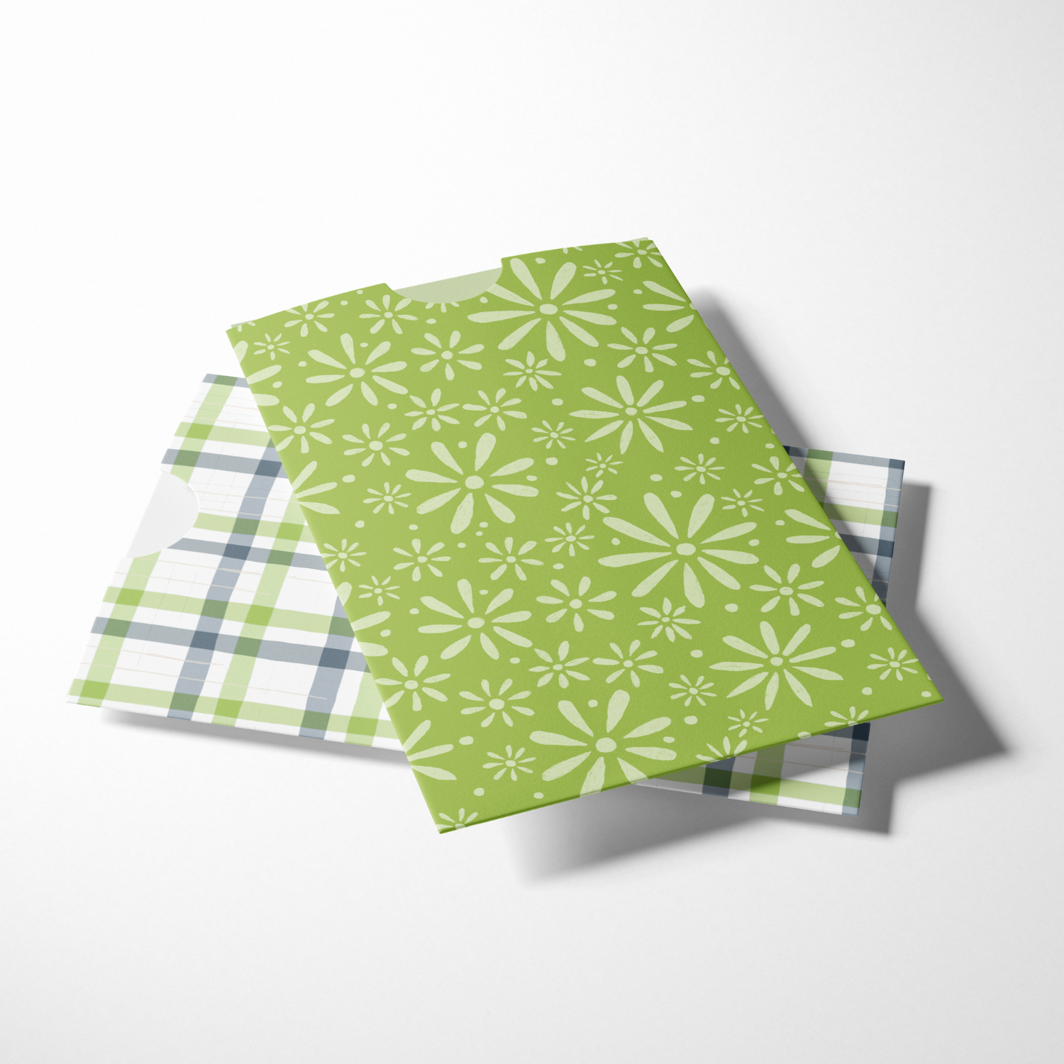 Two patterned paper napkins, one with a green background and white floral design, and the other with a green, gray, and white plaid pattern, placed on a white surface.