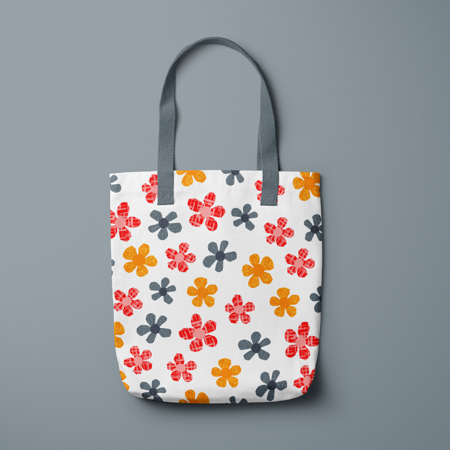 A tote bag with a colorful floral pattern in shades of orange, pink, and gray on a white background hanging against a gray wall.