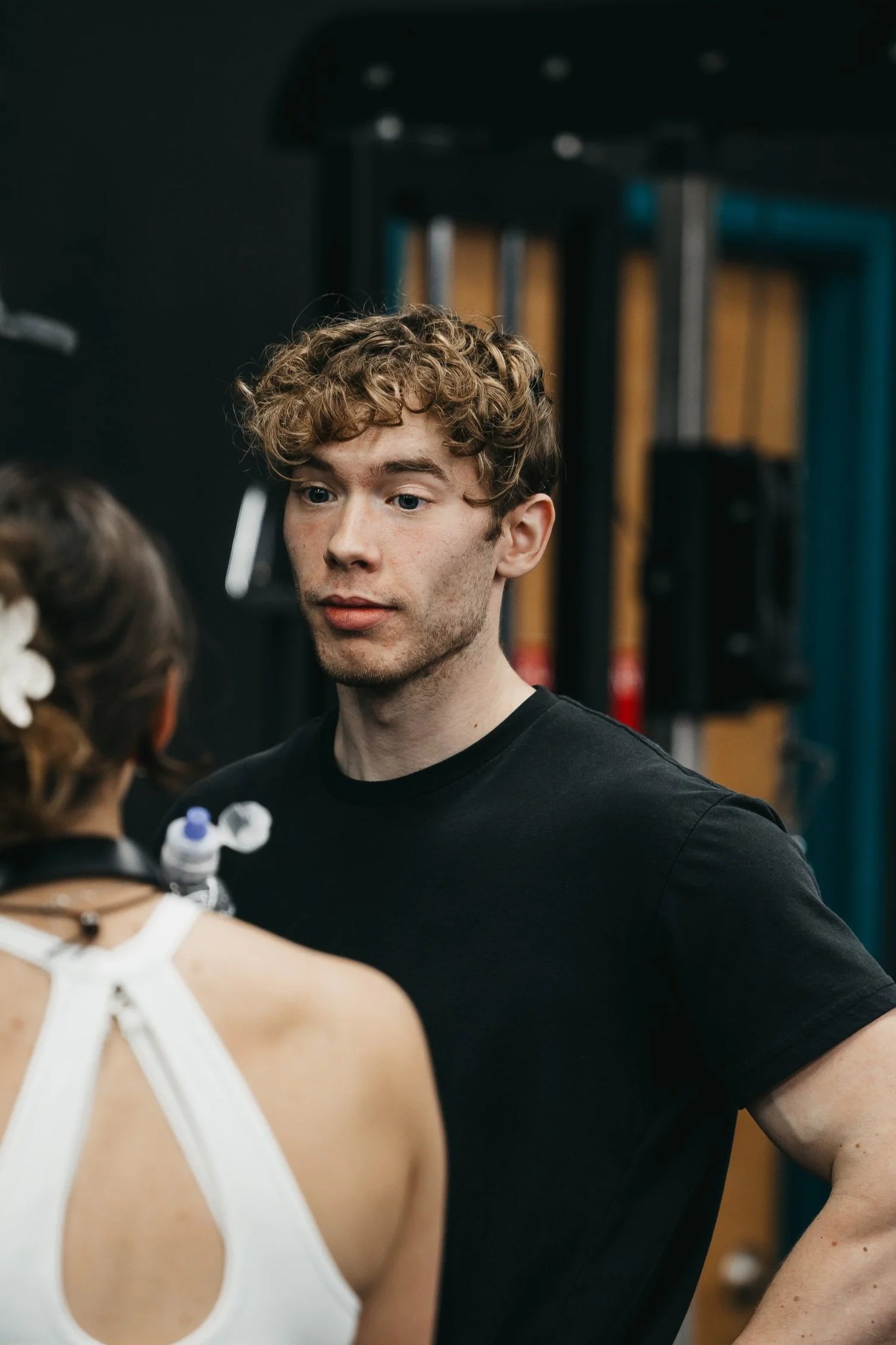 A young man with curly hair listens attentively to a woman with brown hair and a white top.
