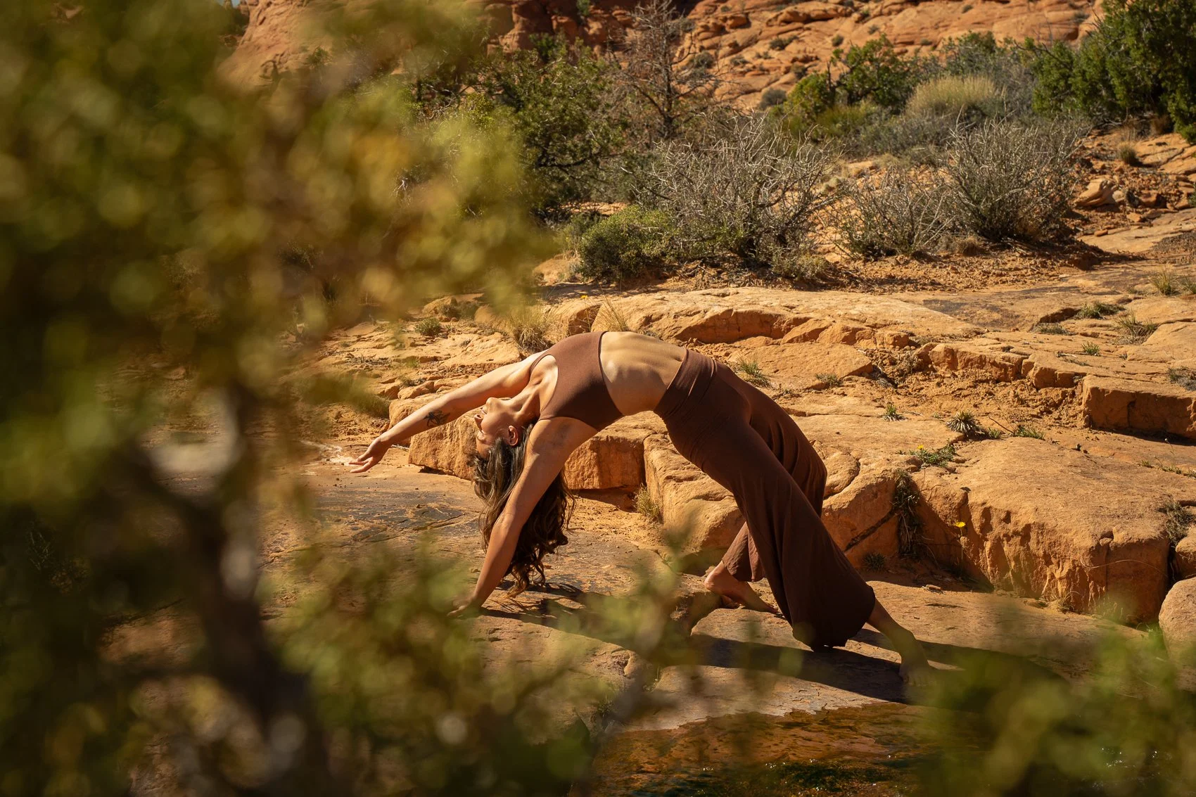 A woman practicing yoga outdoors on rocky terrain in a desert-like landscape, performing a backbend pose.