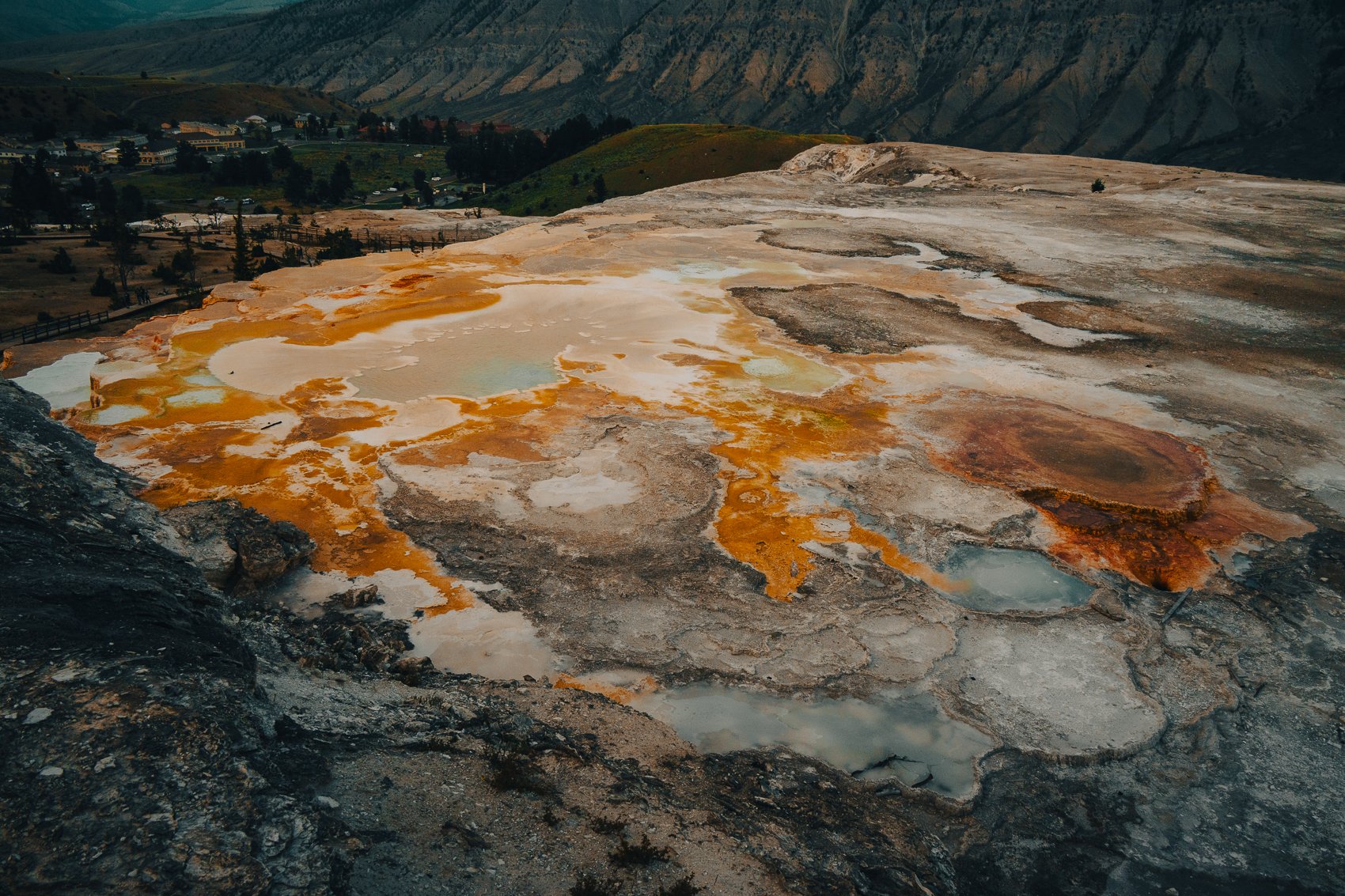 Colorful geothermal hot spring in a rocky landscape with orange, yellow, white, and blue mineral deposits.