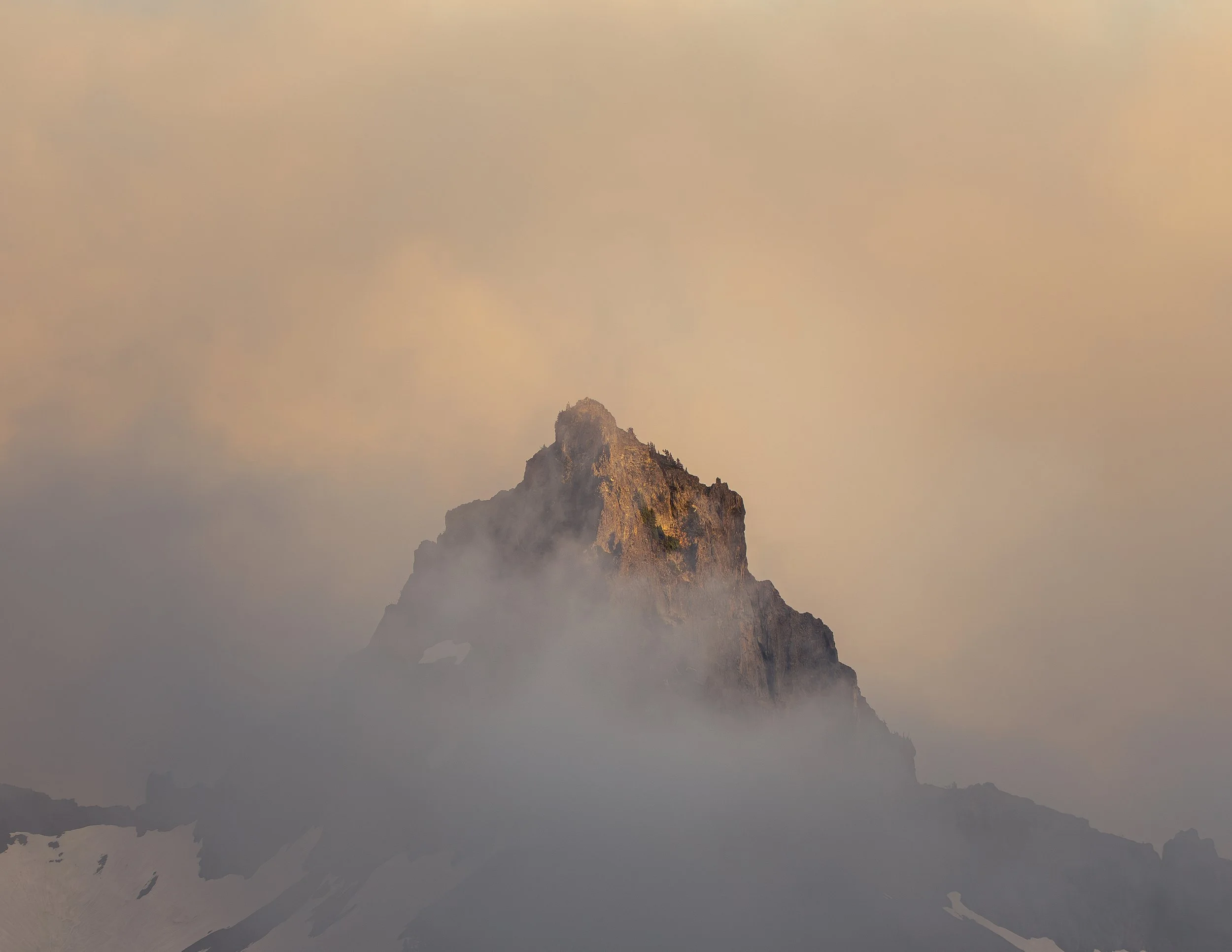 A mountain peak surrounded by fog and clouds during sunrise or sunset.