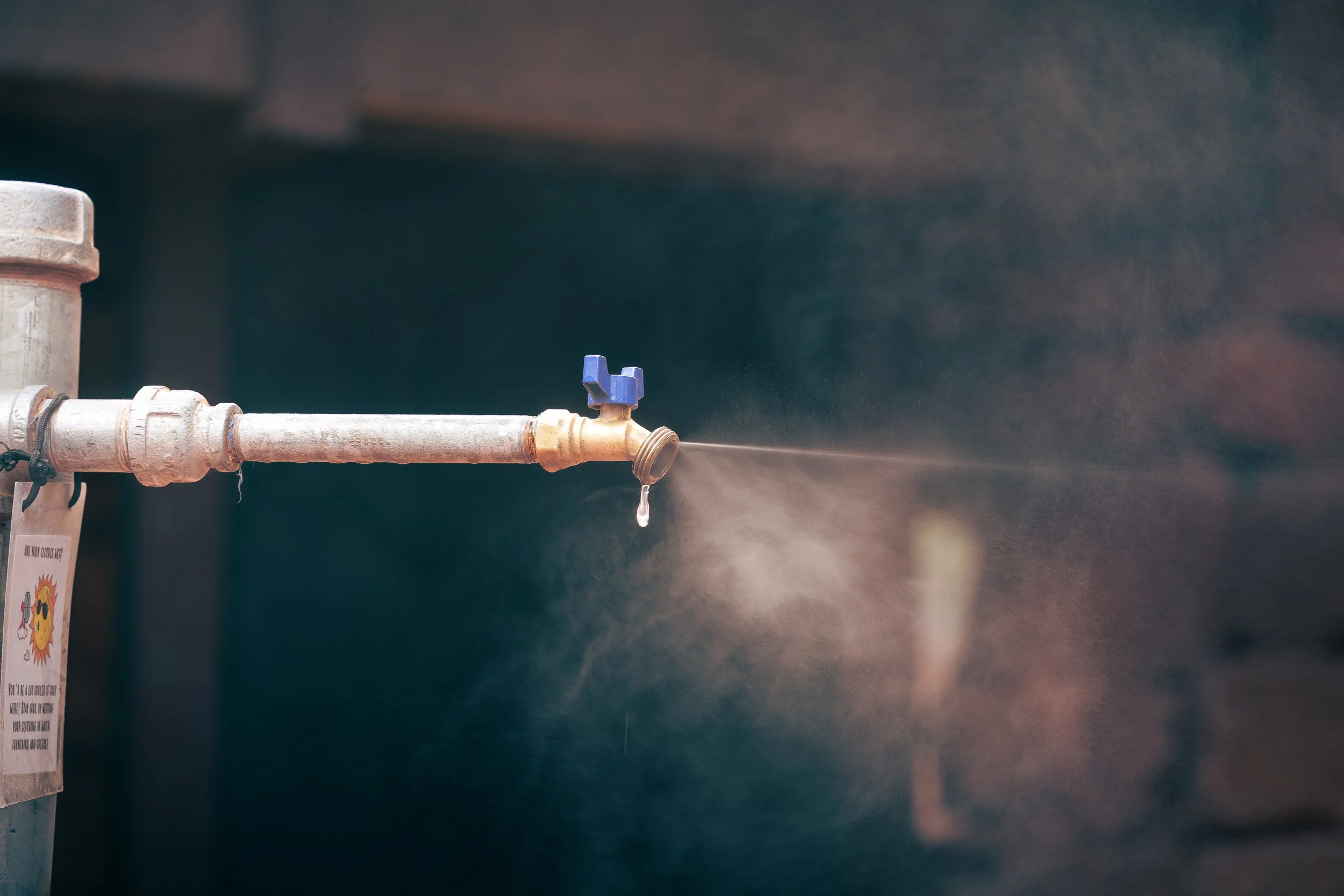 A water faucet attached to a pipe, with water droplets and spray coming out of it.