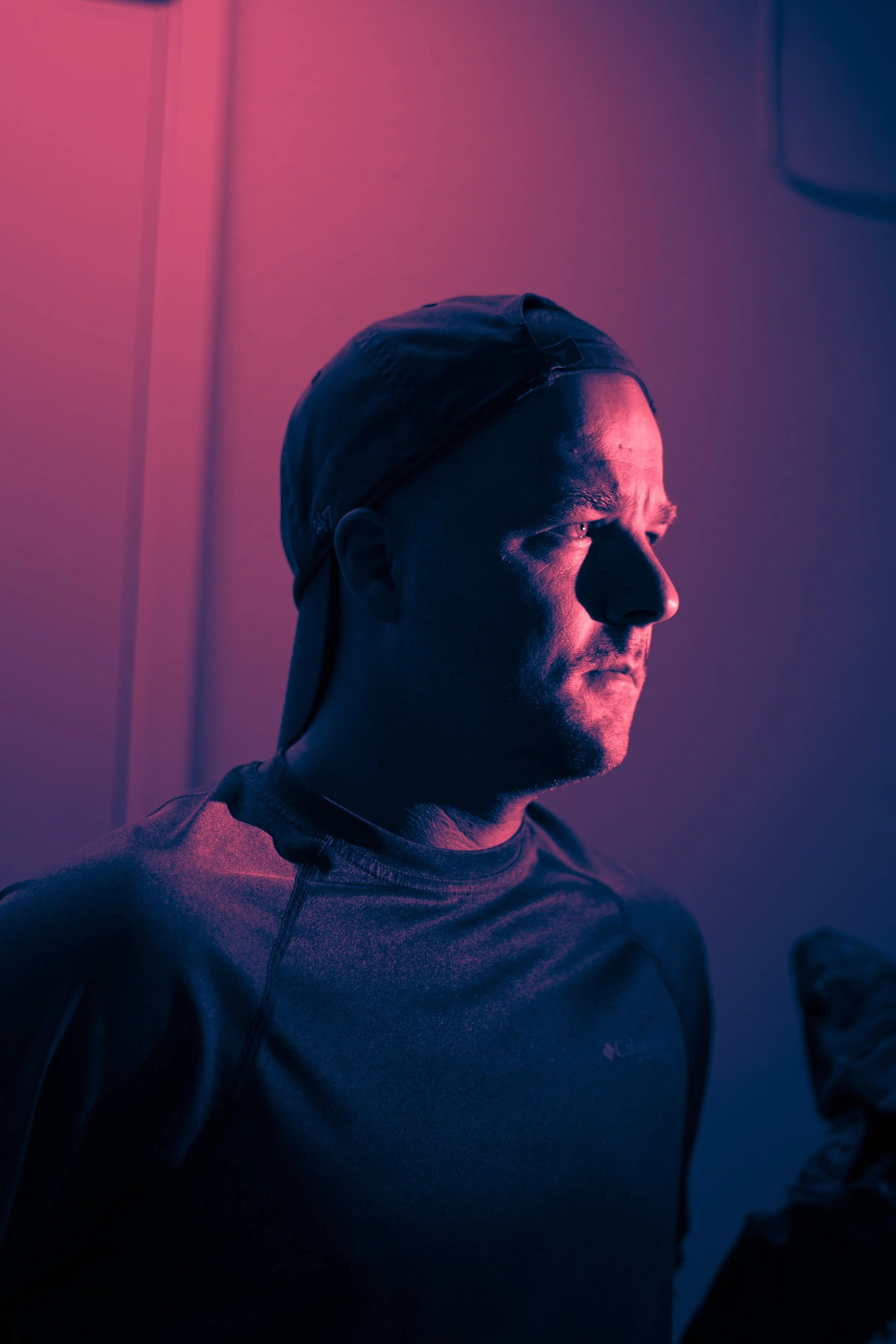A man wearing a cap and sportswear illuminated with pink and blue lighting.