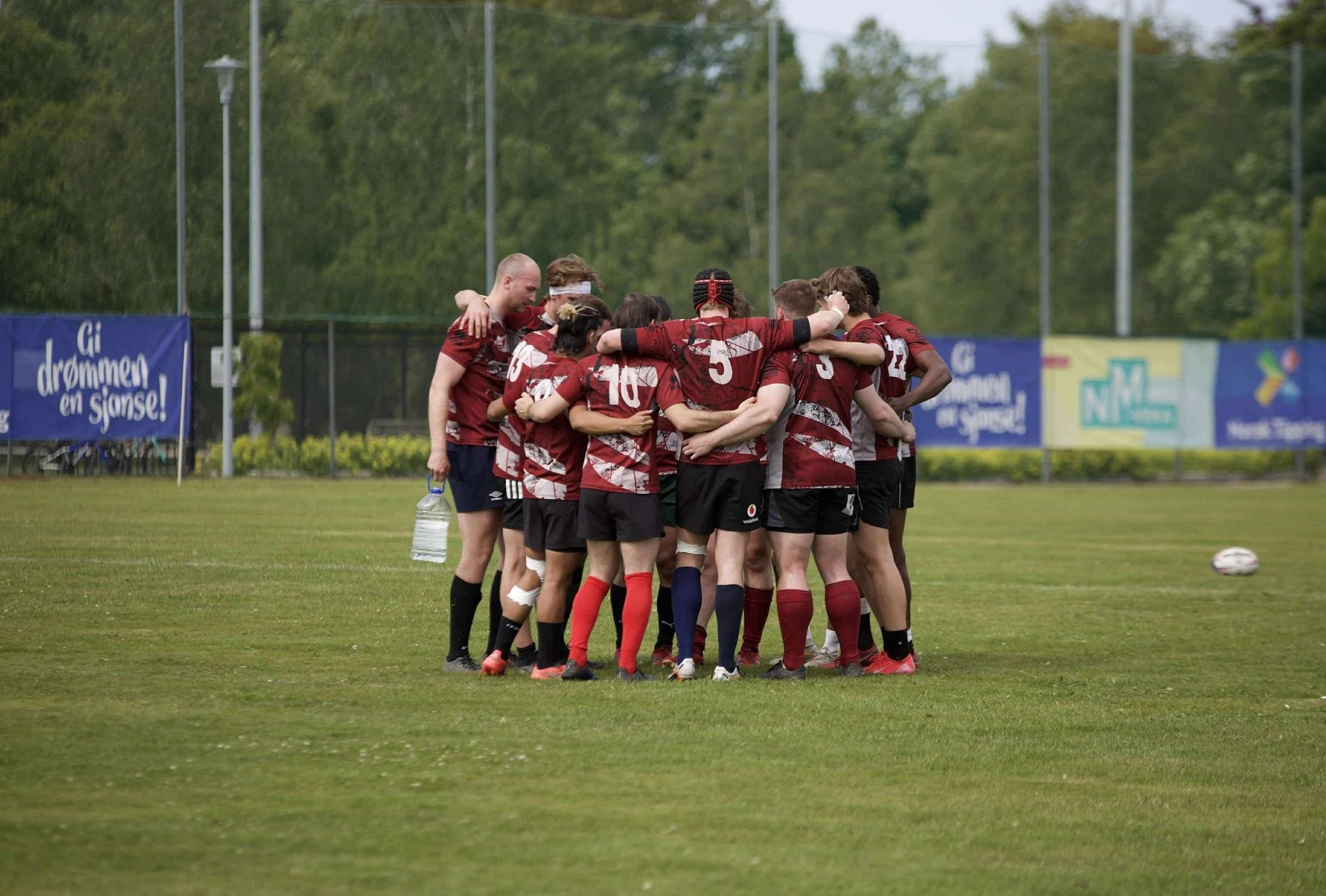 A group of rugby players in red and black uniforms huddle together on a grass field during a game.