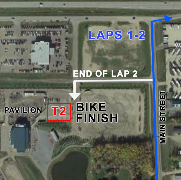 Aerial view of a bike race track with markings and labels indicating lap 1-2, the end of lap 2, and the bike finish line near a pavilion, parking lot, and main street.
