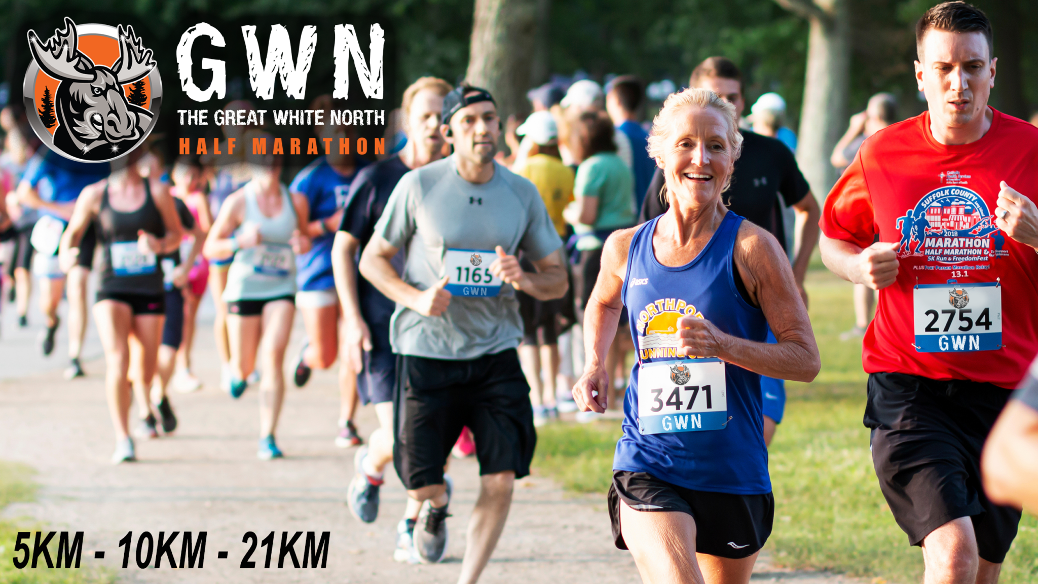Runners participating in the Great White North Half Marathon, with some wearing race bibs and athletic clothing, running on an outdoor trail surrounded by trees.