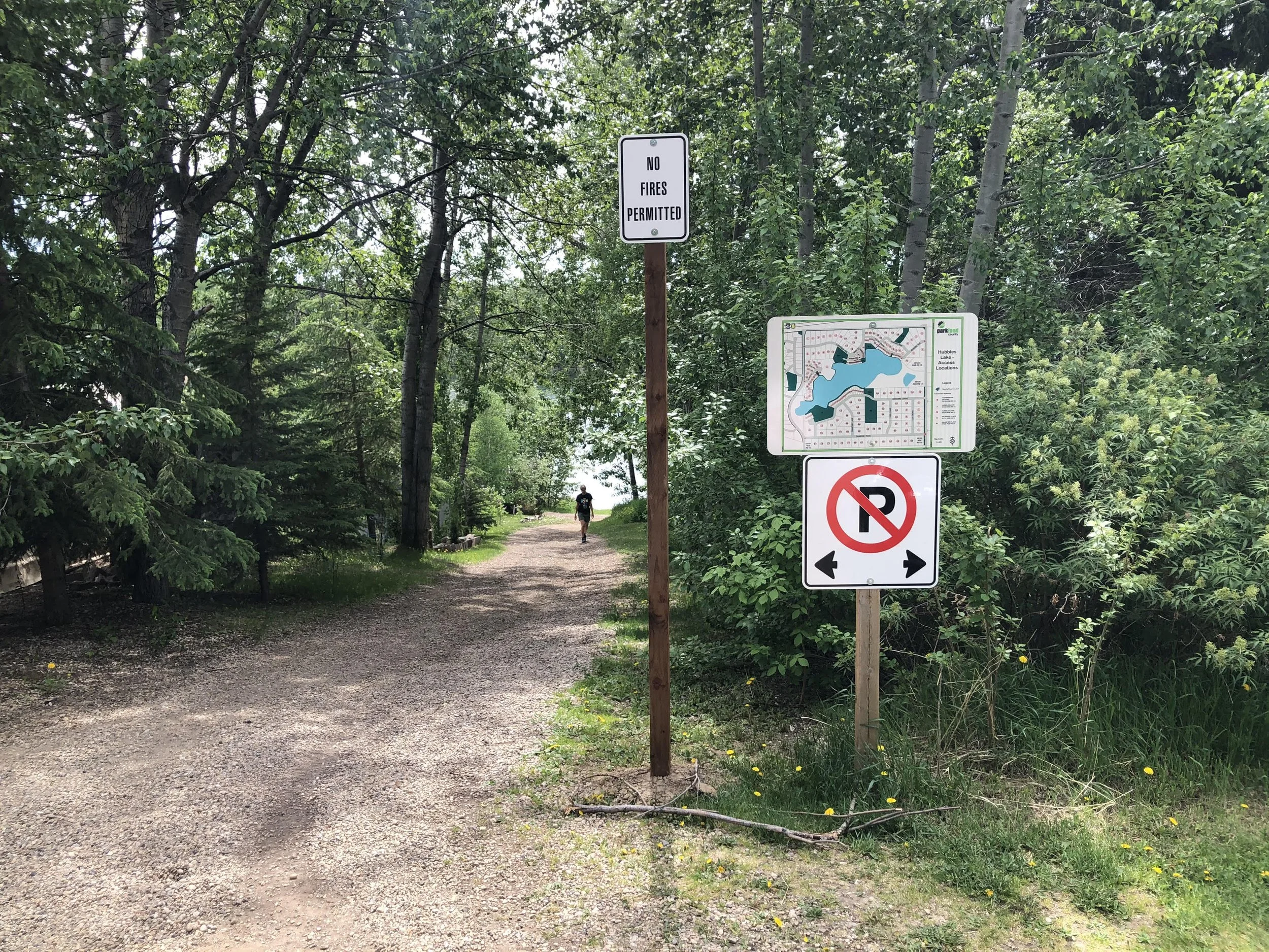 A dirt trail in a forested area with multiple signs, including one that says 'No Fires Permitted' and a map of the park.