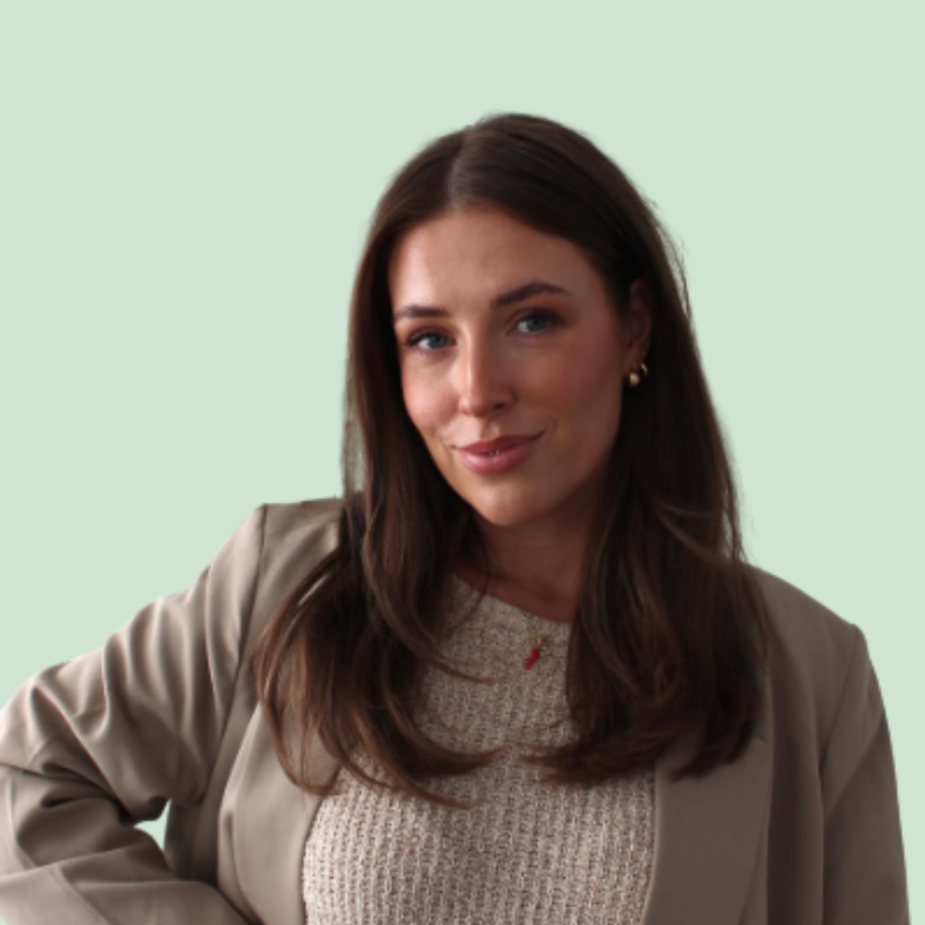 Close-up image of a woman with long brown hair, wearing a beige blazer over a beige sweater, standing against a light green background.