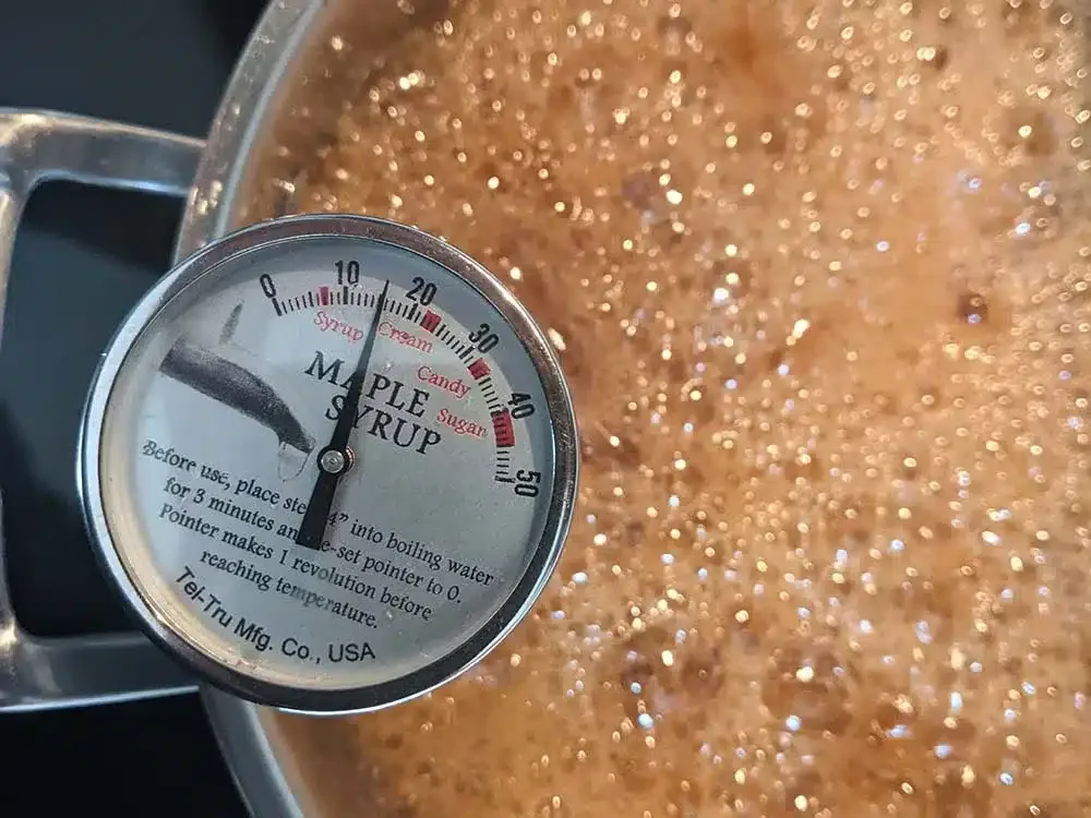 A meat thermometer indicating a temperature of approximately 10 degrees Fahrenheit, submerged in a bubbling mixture of caramel sauce in a pot.