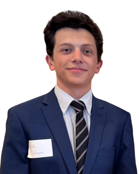 Young man in a navy blue suit, light dress shirt, and striped tie, smiling, standing against a white background, with a name tag on his suit.