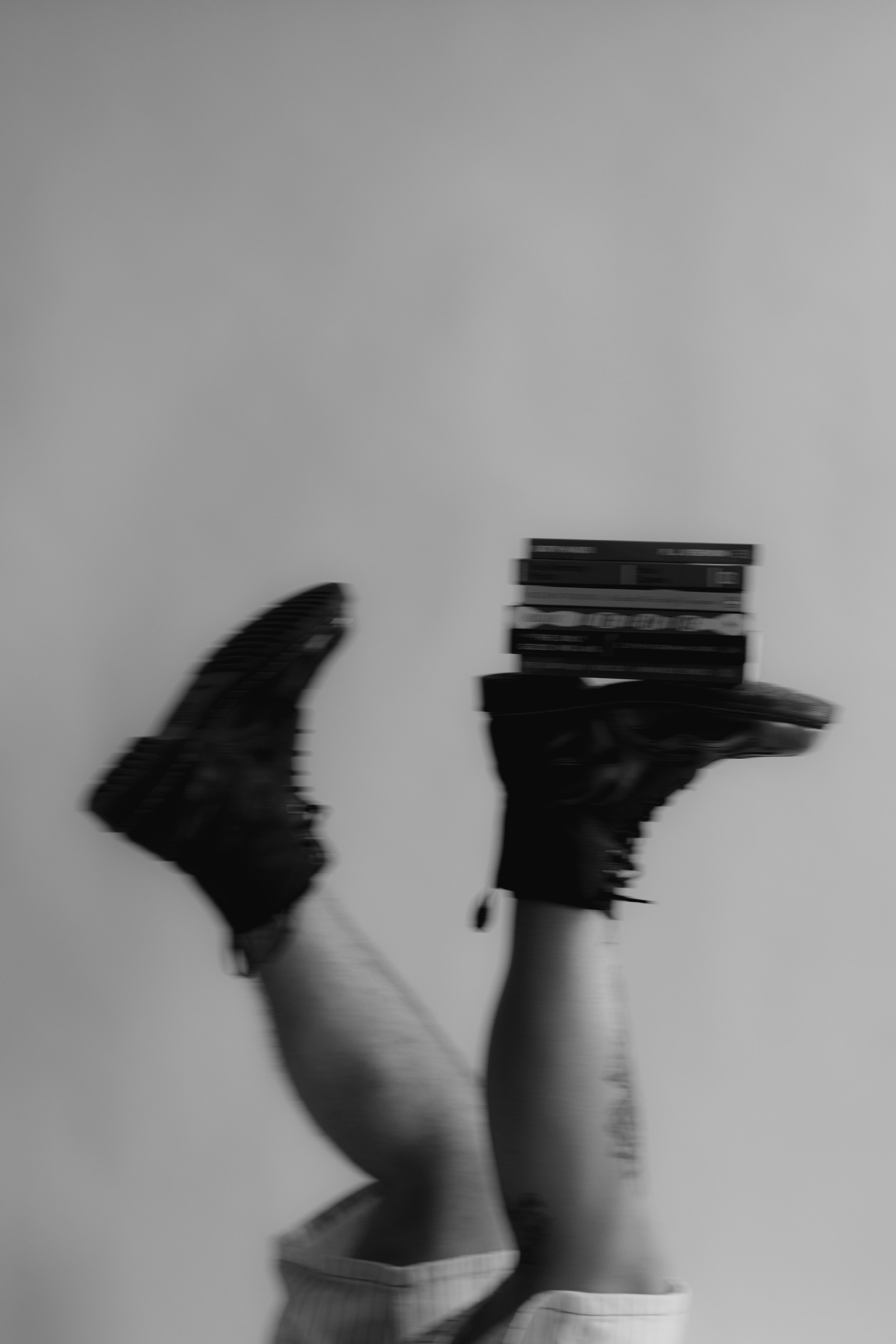 A person wearing striped socks and sneakers, holding a stack of books, with a plain background.