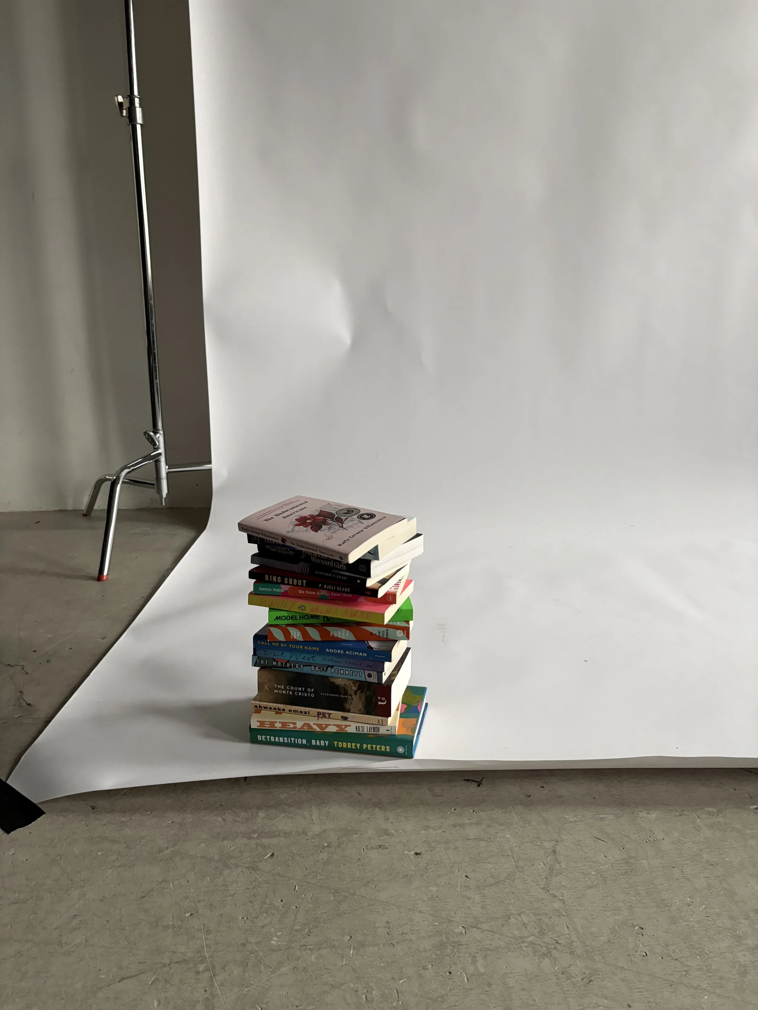 Stacked books on a white backdrop, with a lighting stand to the left in an indoor setting.