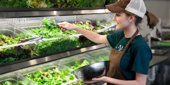 A woman in an apron picks up a vibrant salad, showcasing Verde's dedication to fresh, healthy dining in Charleston, SC.