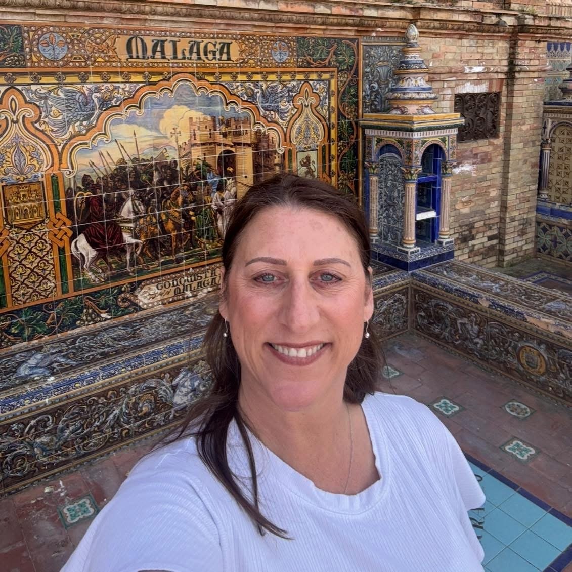 A woman taking a selfie in front of decorative tiled artwork and architecture.