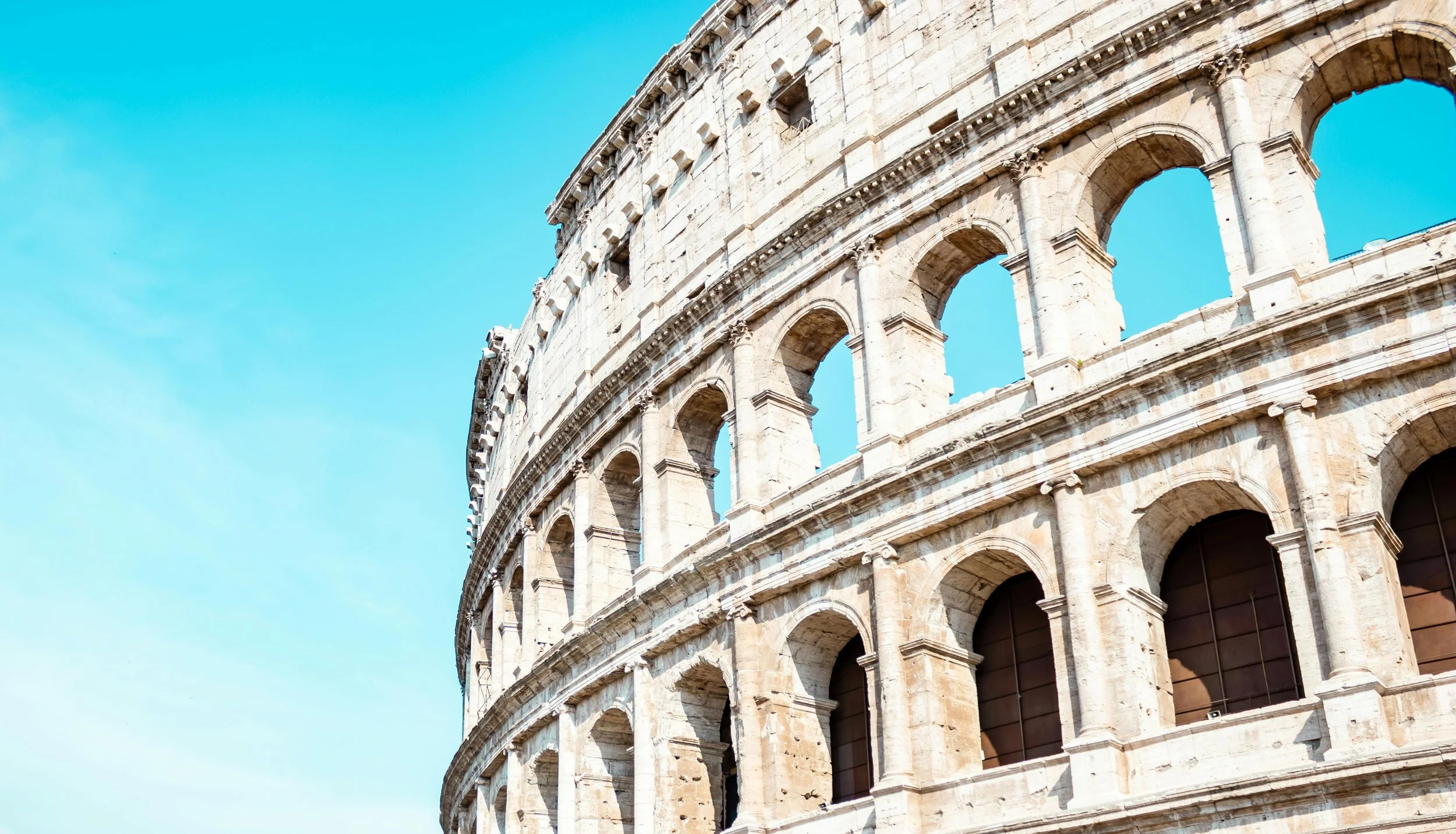 Close-up of the exterior of the Roman Colosseum showing its arches and stones against a blue sky.