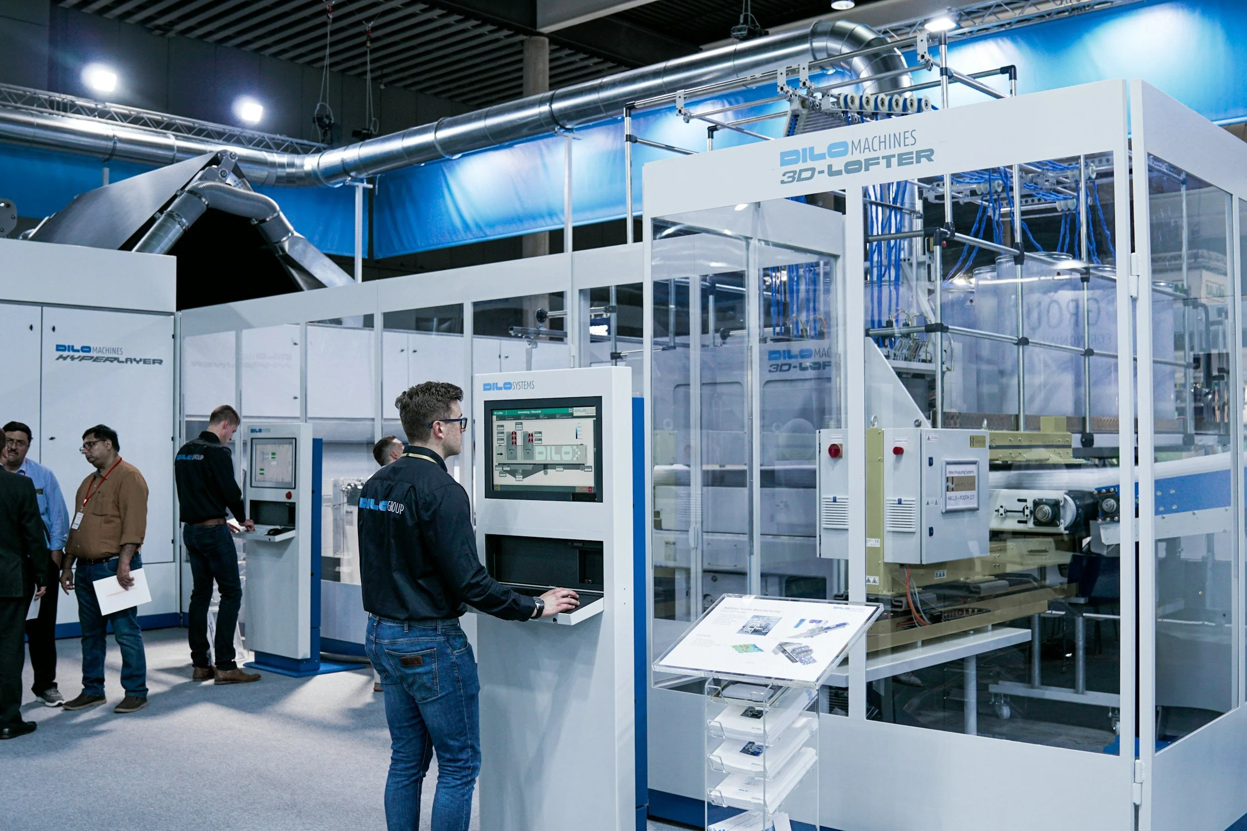 industrial machinery, a 3D-laminator, several staff observing and interacting with the equipment.