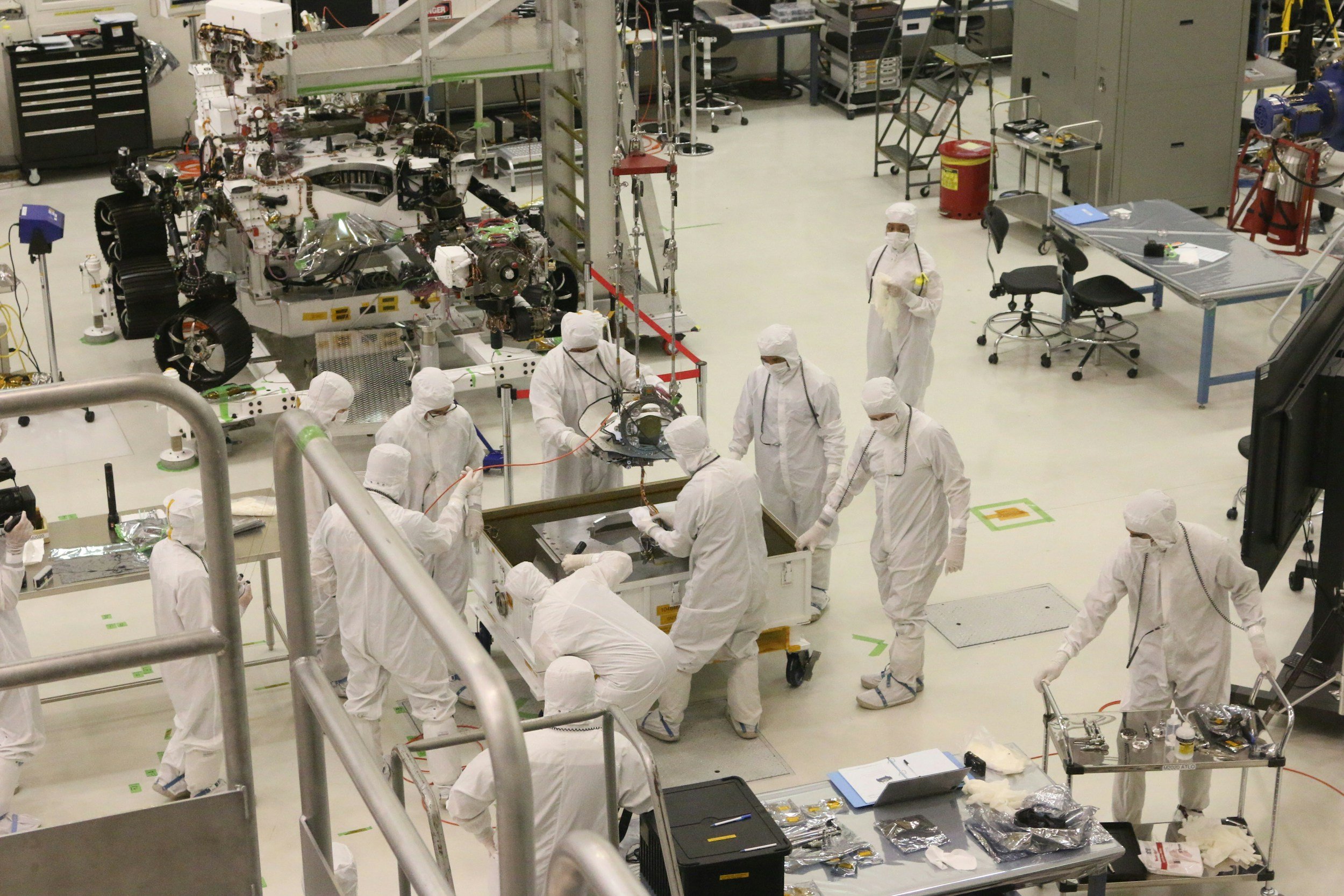 Technicians in Tyvek suits and breathing masks working in a high-tech manufacturing facility.