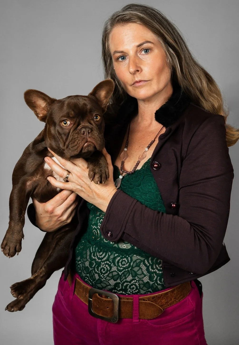 Olivia from Le Epitome Kennels in Waikato, New Zealand, holding Nyx, a chocolate coloured French Bulldog breeding female, against a plain grey background.