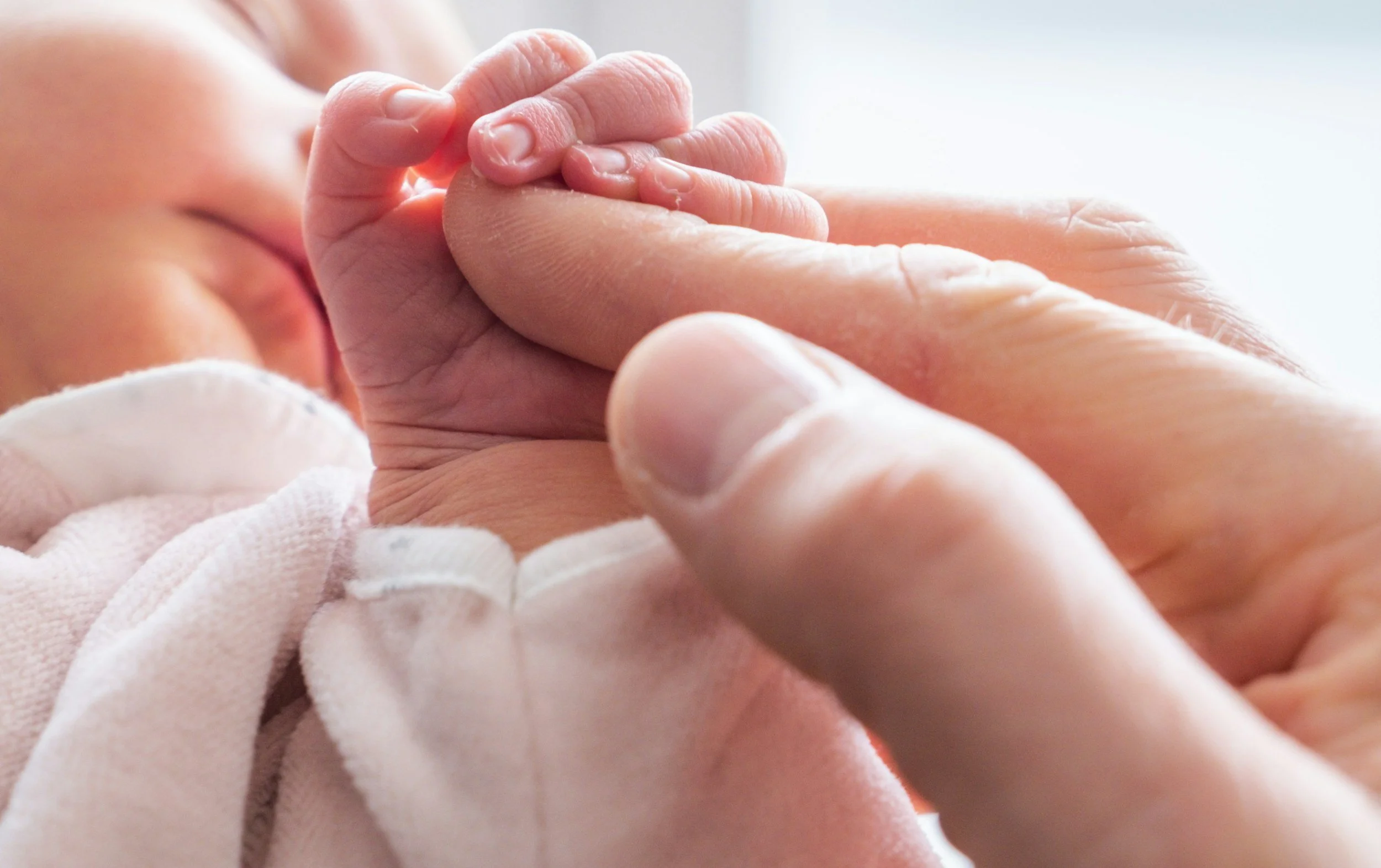 Newborn baby holding a parent's finger, symbolising connection, attachment and support during the fourth trimester.
