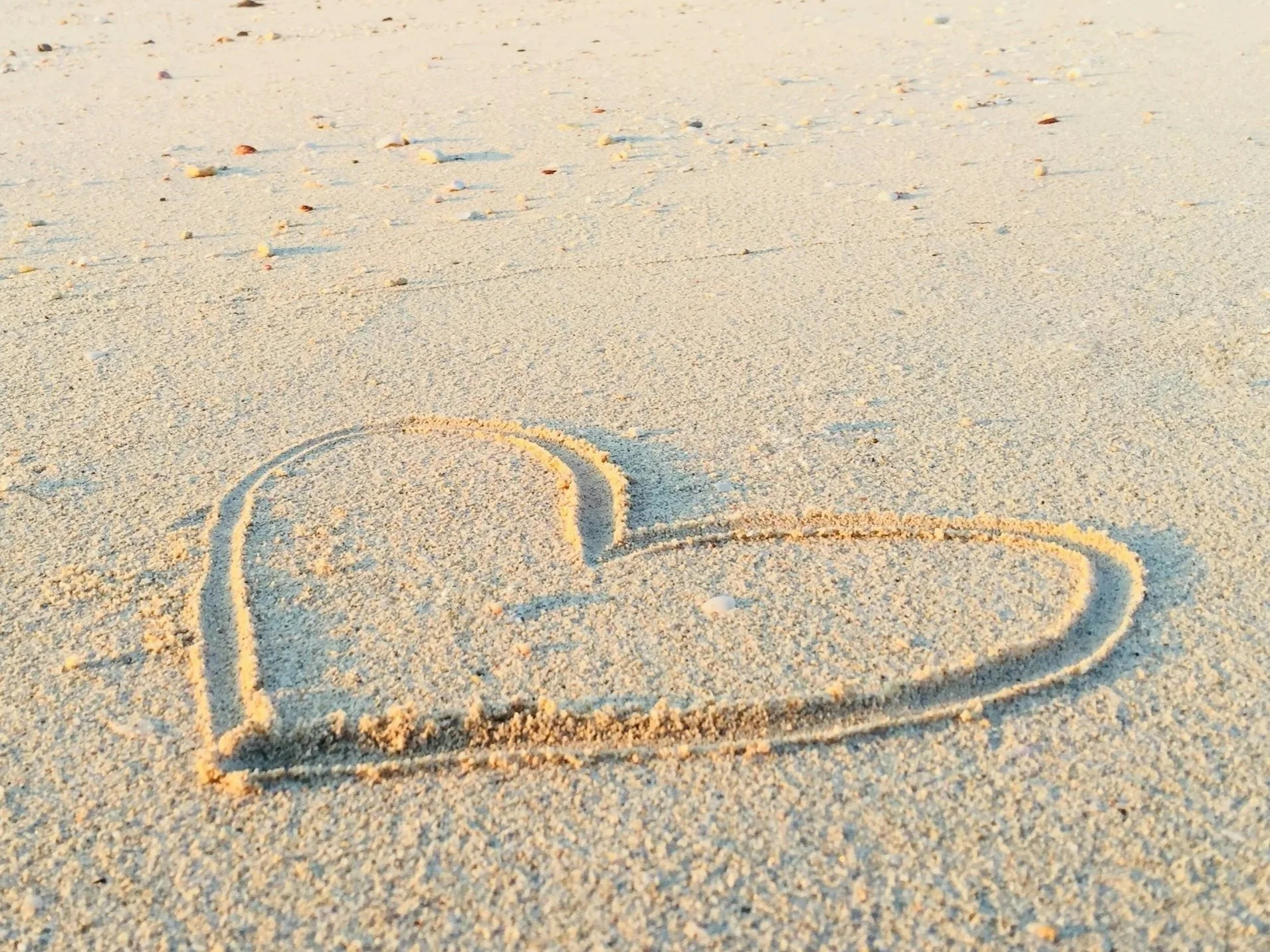 Heart drawn in the sand on a Sunshine Coast beach, representing compassion, connection and support throughout pregnancy, postpartum and parenthood.