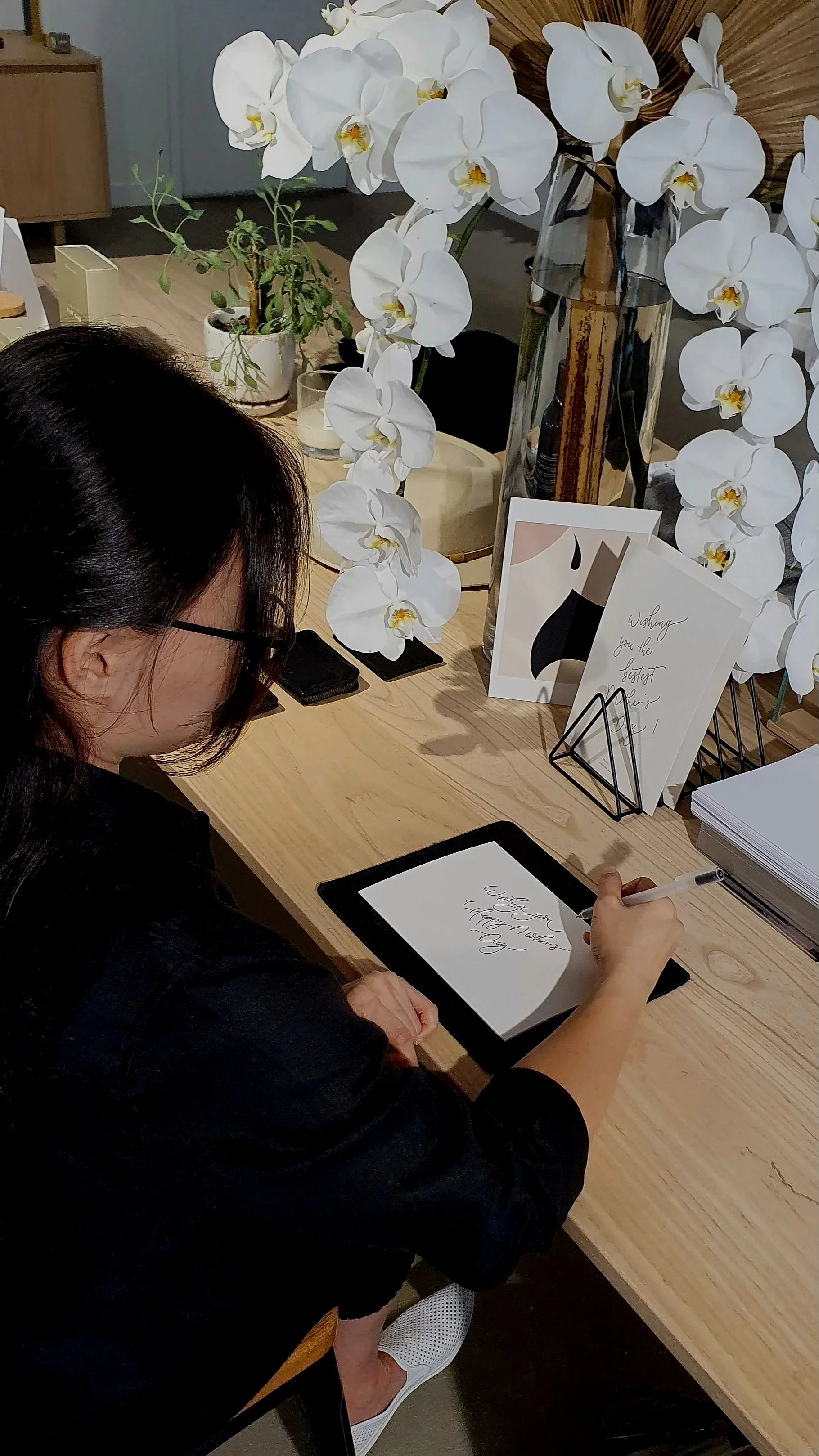 Gold Coast calligrapher Sheeling performing live calligraphy at an event, writing at a styled table with white orchids