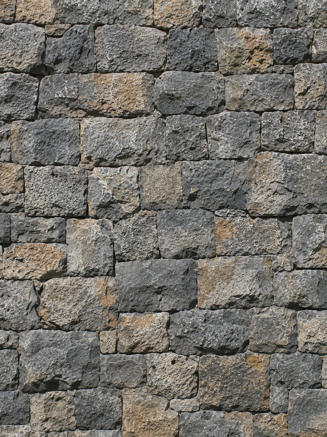 Close-up of a stone wall made of rectangular gray and tan stones with rough textures.