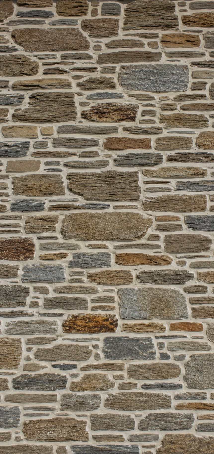Close-up of a stone brick wall with various shades of brown and gray stones and beige mortar.