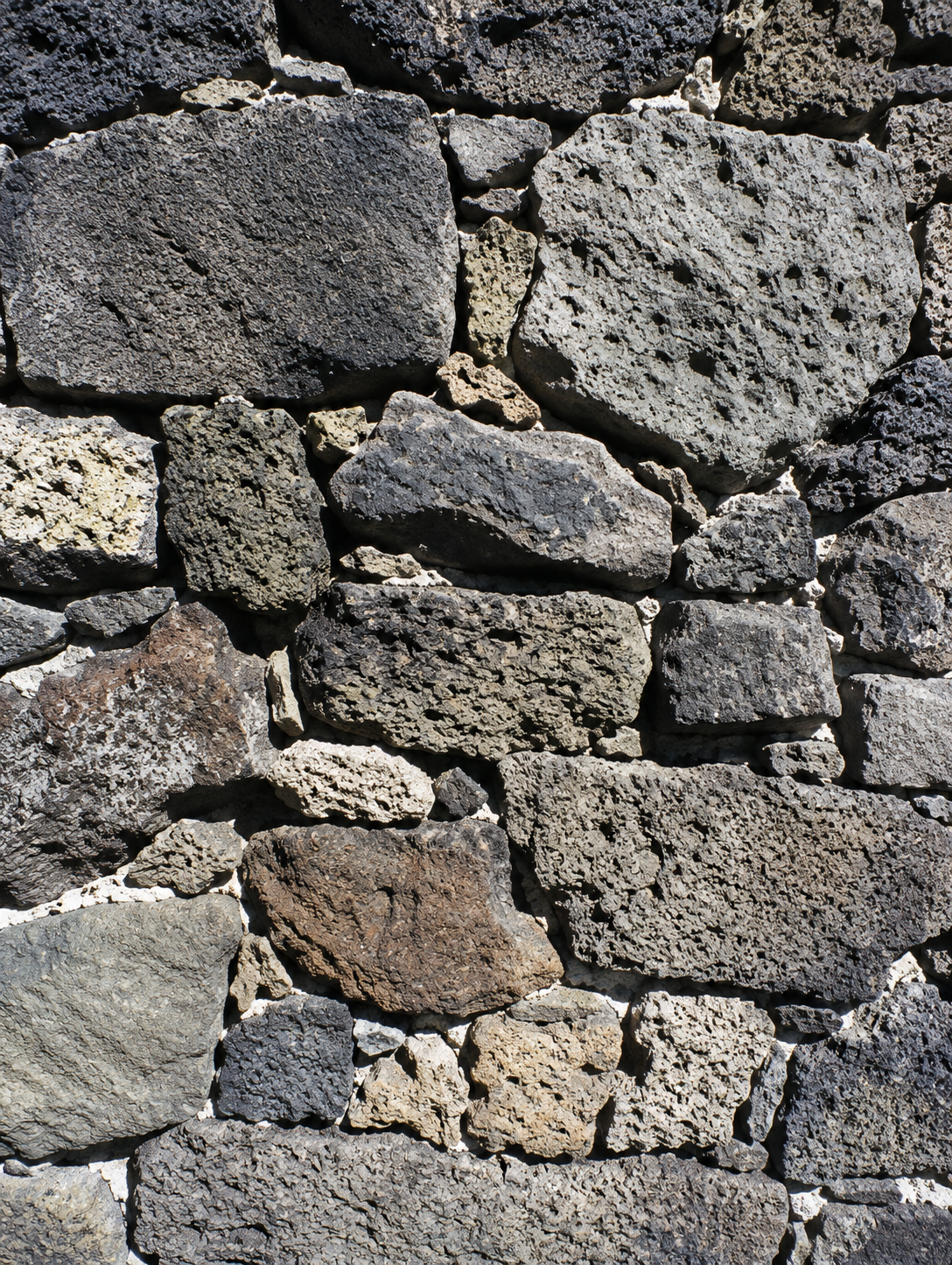 Close-up of a stone wall with various irregularly shaped gray and brown stones.