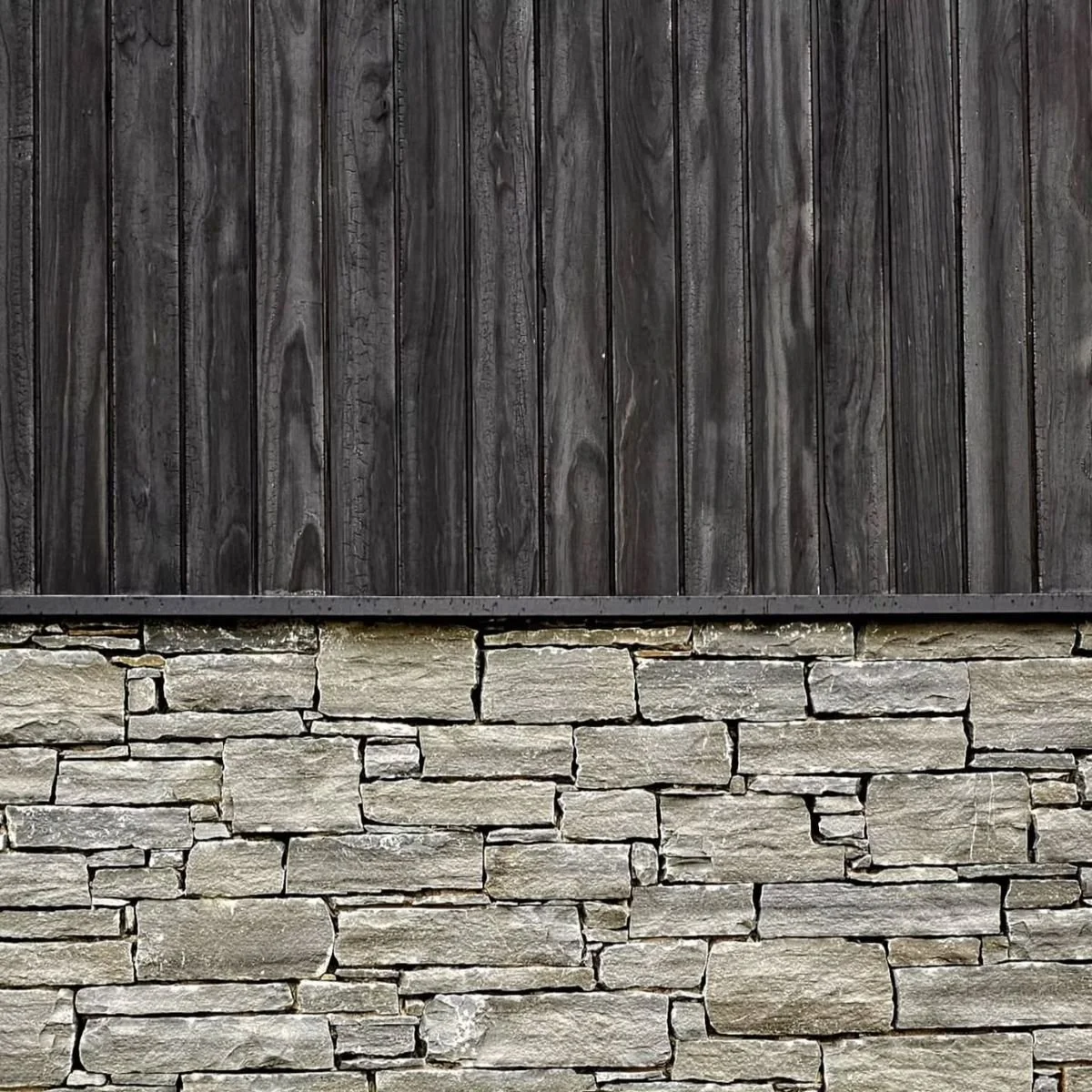 Close-up of a wall with dark wooden planks above a section of gray stone bricks.