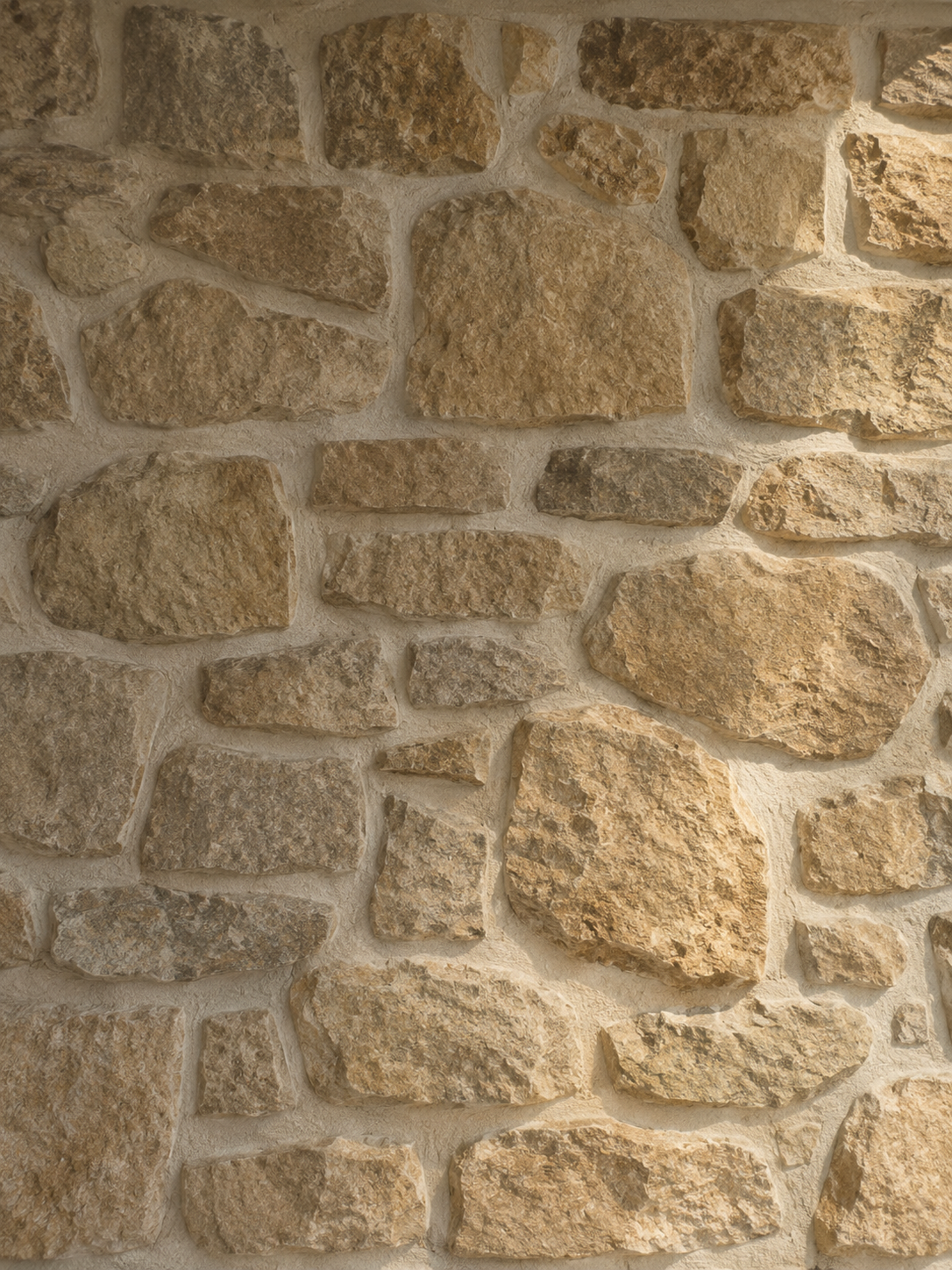 A close-up of a beige stone brick wall with rough texture and mortar joints.