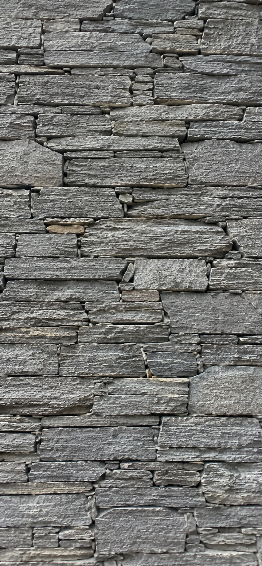Close-up view of a stacked stone wall with irregularly shaped gray stones aligned horizontally.