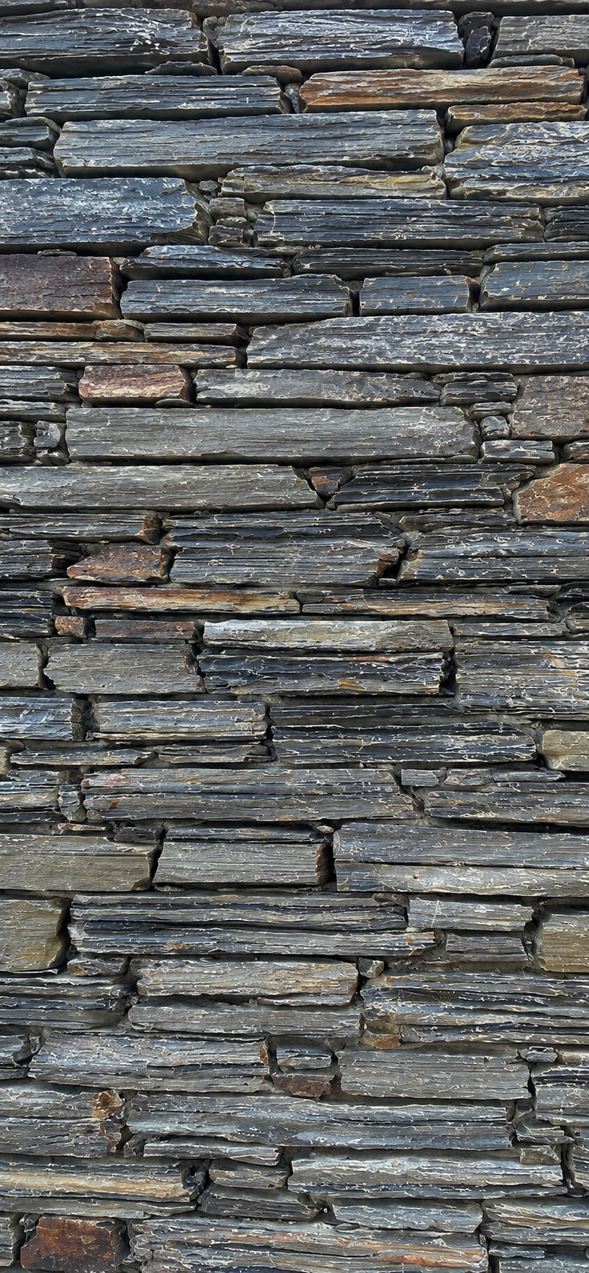 Close-up of a stacked stone wall made of thin, flat, dark gray and brown rocks.