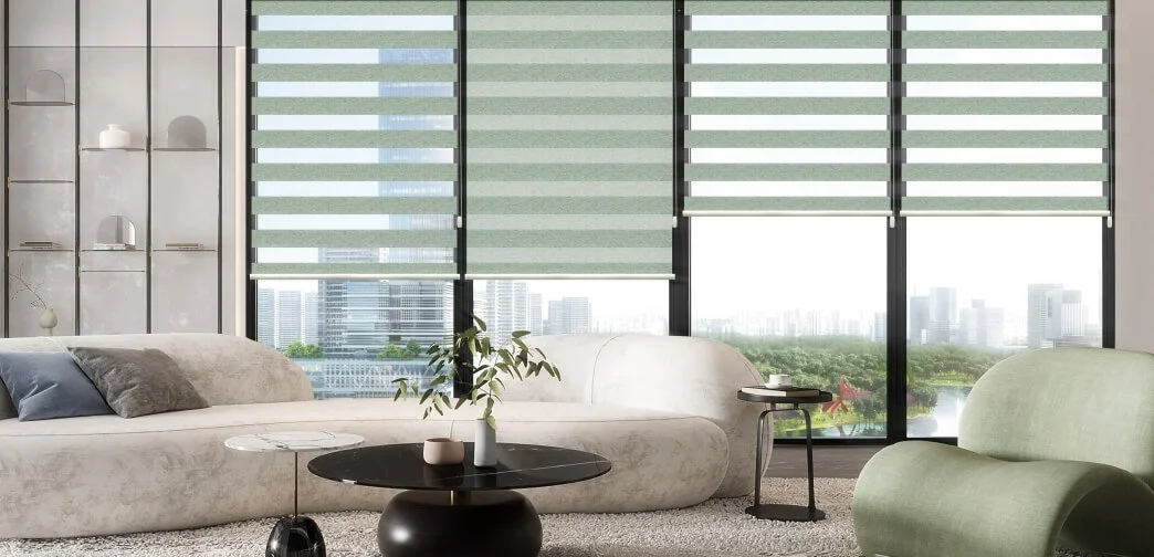 Modern living room with large windows, cityscape view, beige sofa, green chair, round black coffee table, small side tables, and decorative objects.