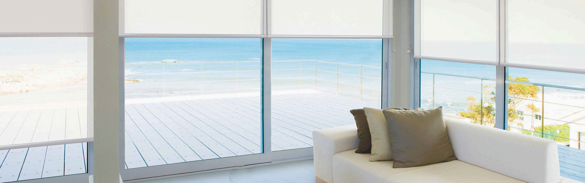 Living room with a white sofa and pillows facing large glass sliding doors leading to a balcony with an ocean view.
