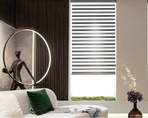 Modern living room with a white cushioned sofa, a green pillow, a black and white throw blanket, a decorative sculpture with a hoop, a large painting, and a window with shades.