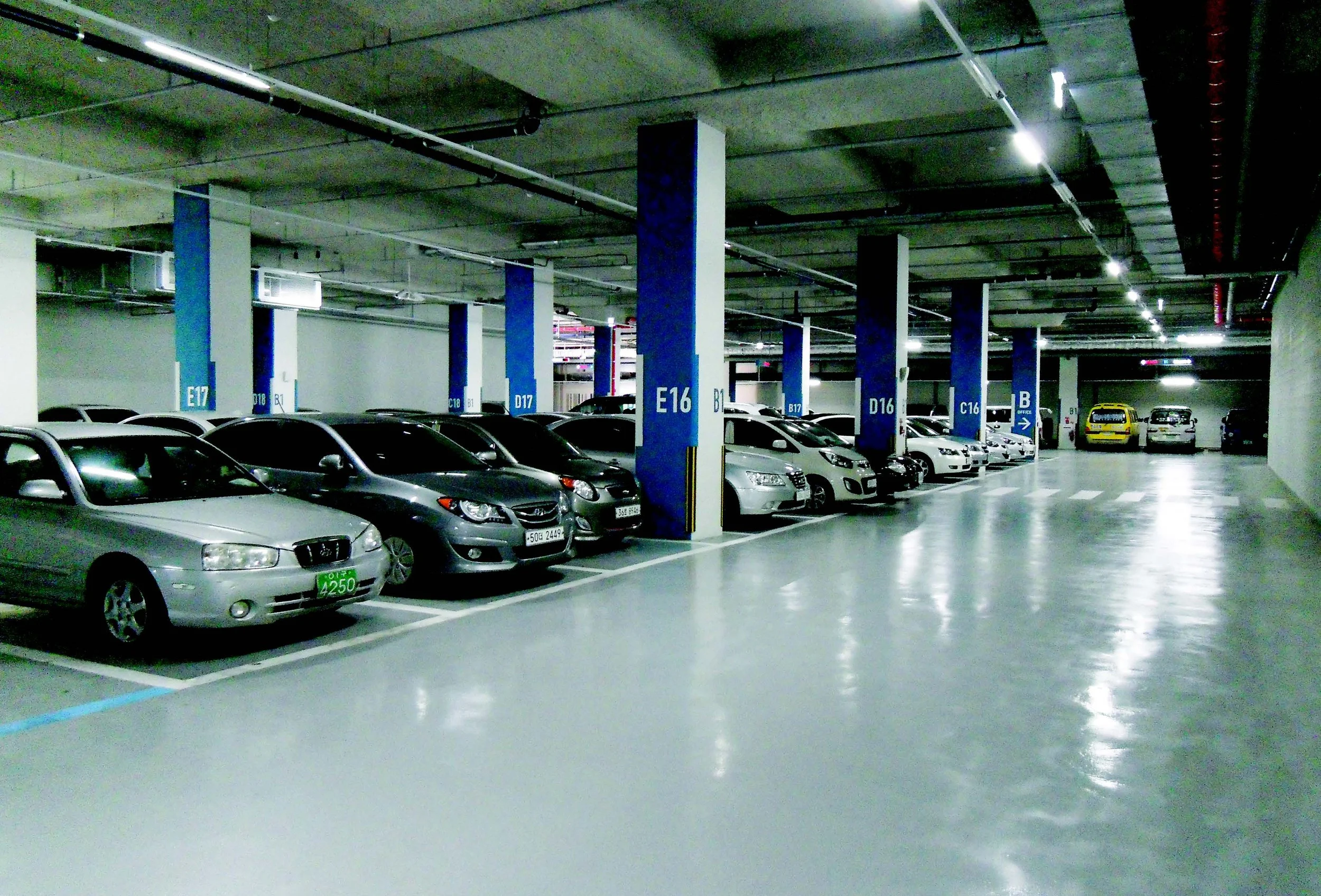 Underground parking garage with multiple parked cars, concrete pillars, and overhead lighting.
